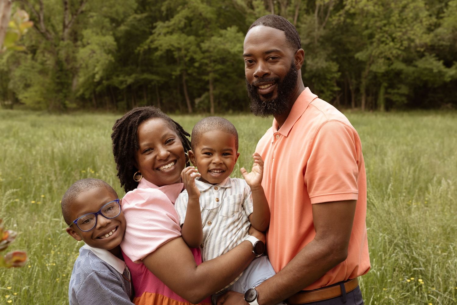 Happy family sharing joyful moments together while embracing in a lush green field on a sunny day.