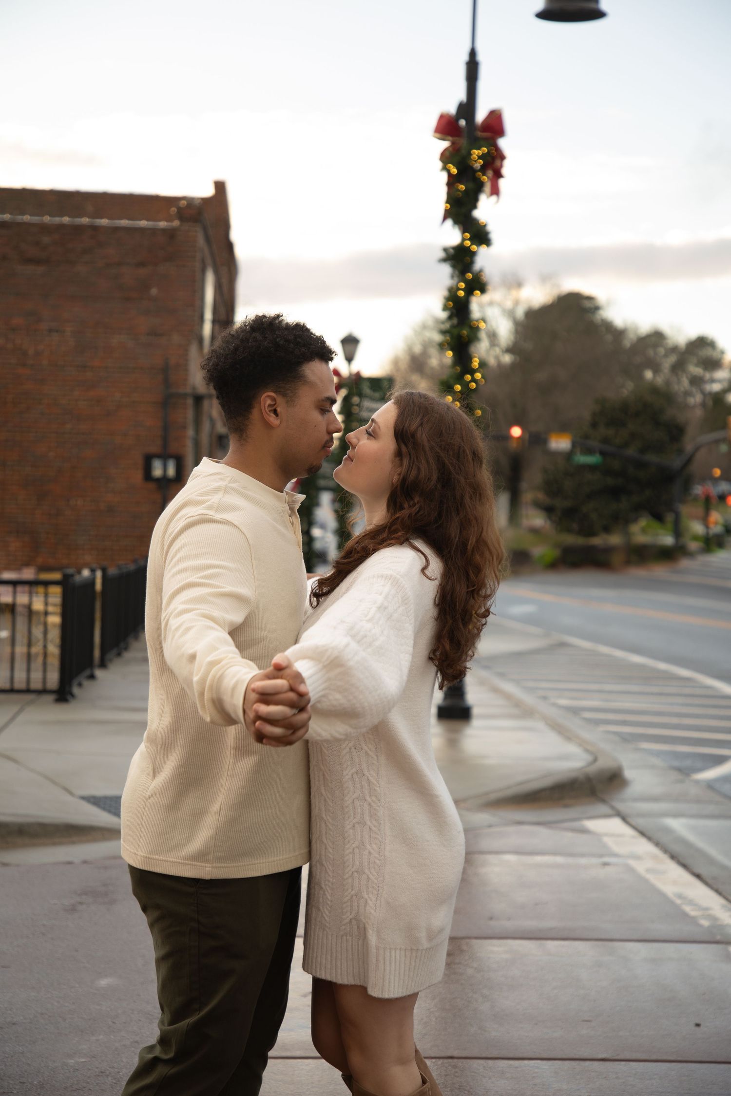 Couple shares a romantic moment under holiday decorations on a quiet street at dusk.