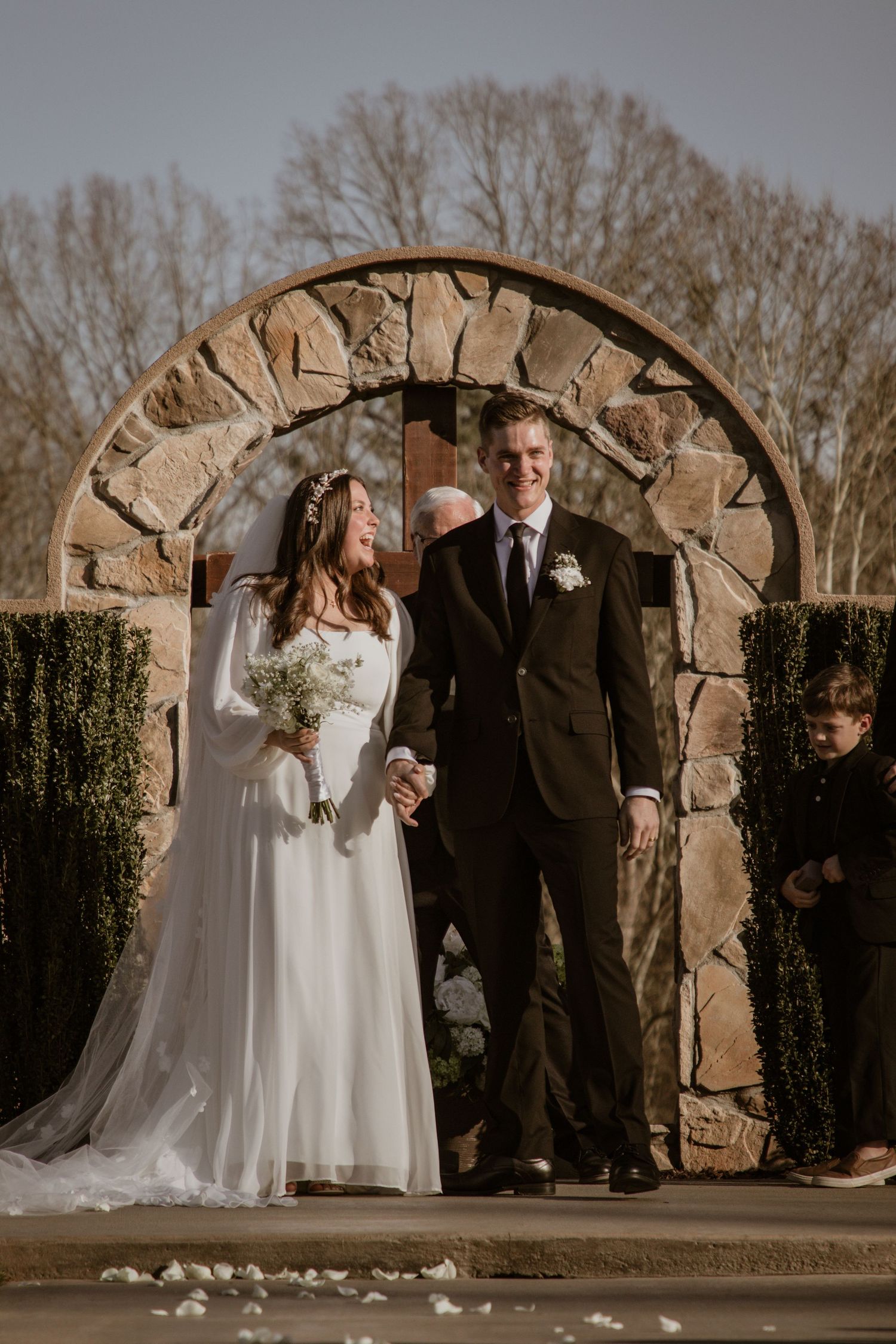 Bride and groom standing under a stone archway during their wedding ceremony.