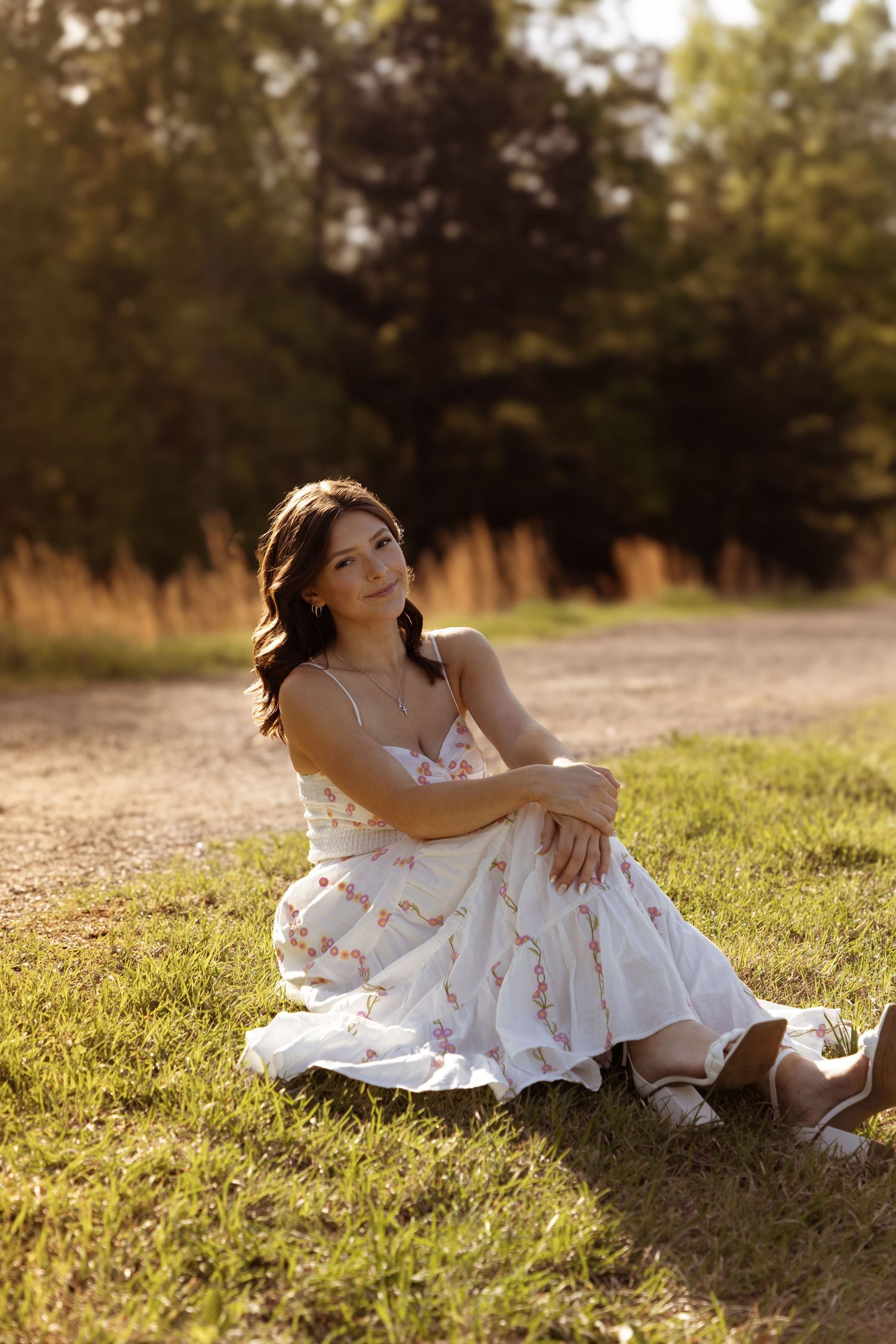 A person in a white floral dress reclines on sunlit grass during a warm summer day.