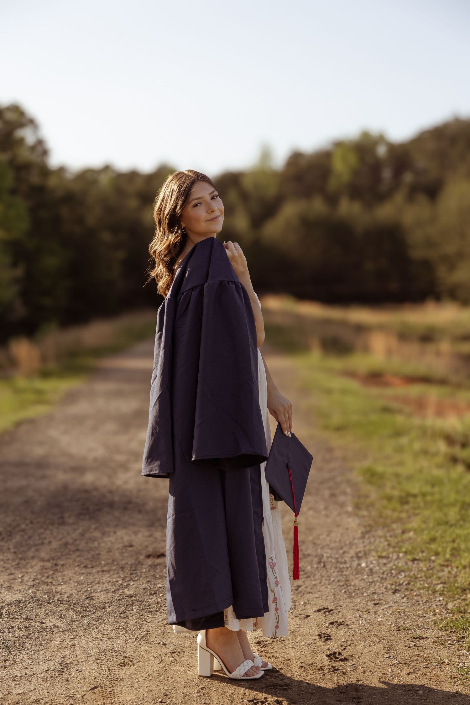Child stands in navy coat and shoes on a dirt path in evening sunlight.