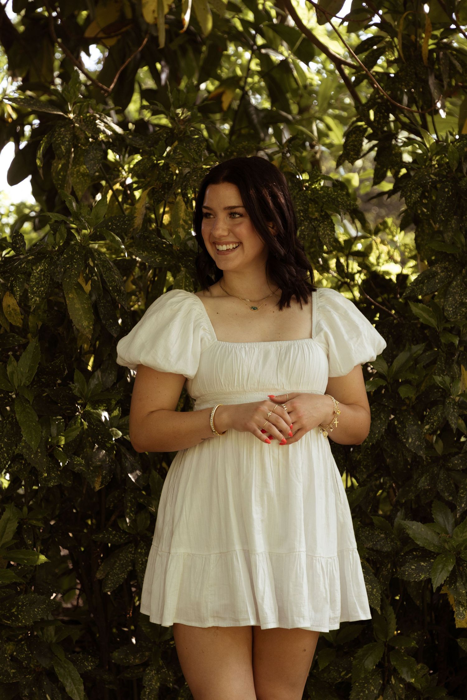 A white summer dress with puff sleeves is photographed against lush green foliage in natural lighting.