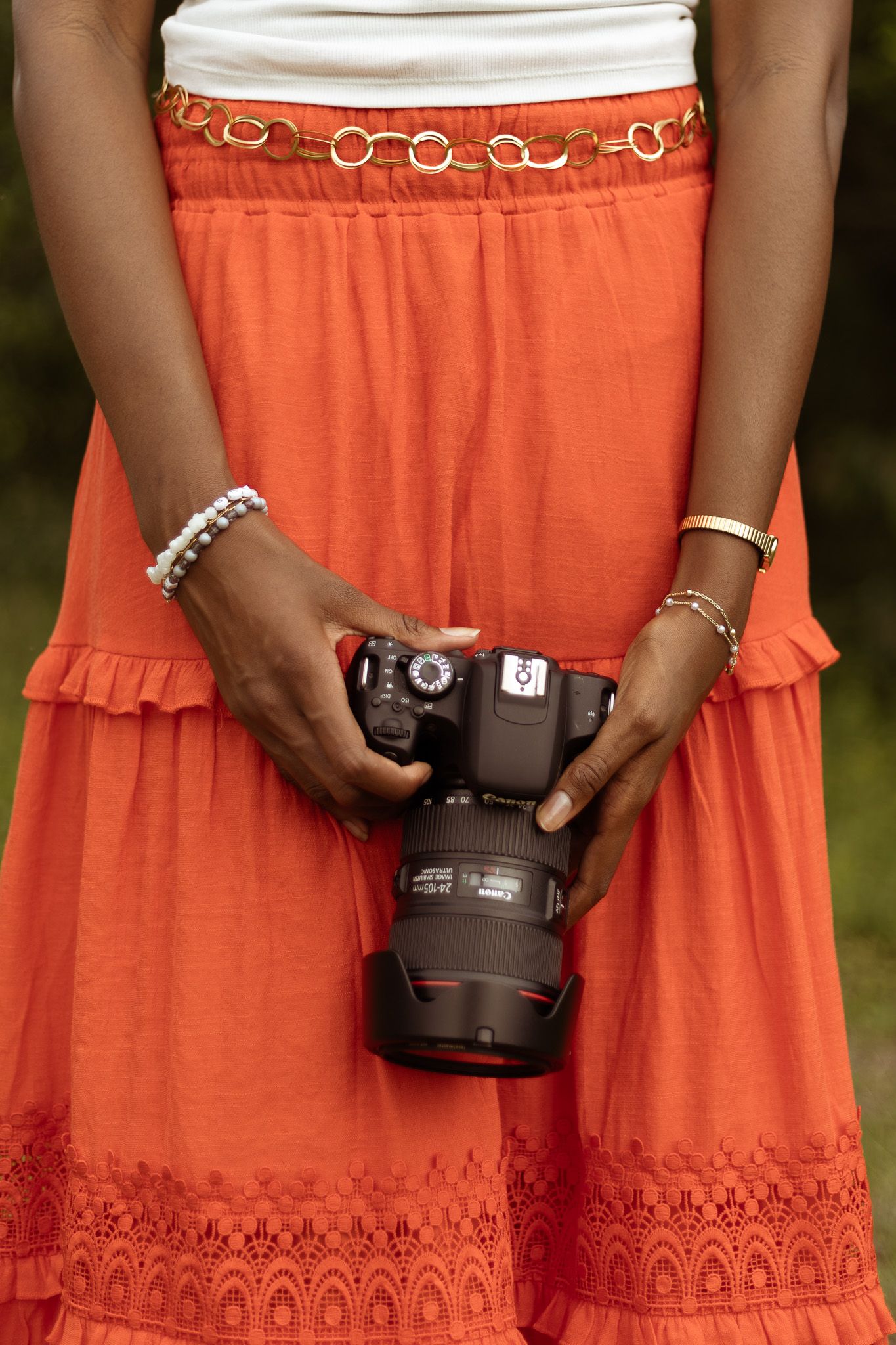 Hands holding DSLR camera in front of orange dress with embroidered hem and decorative belt detail.
