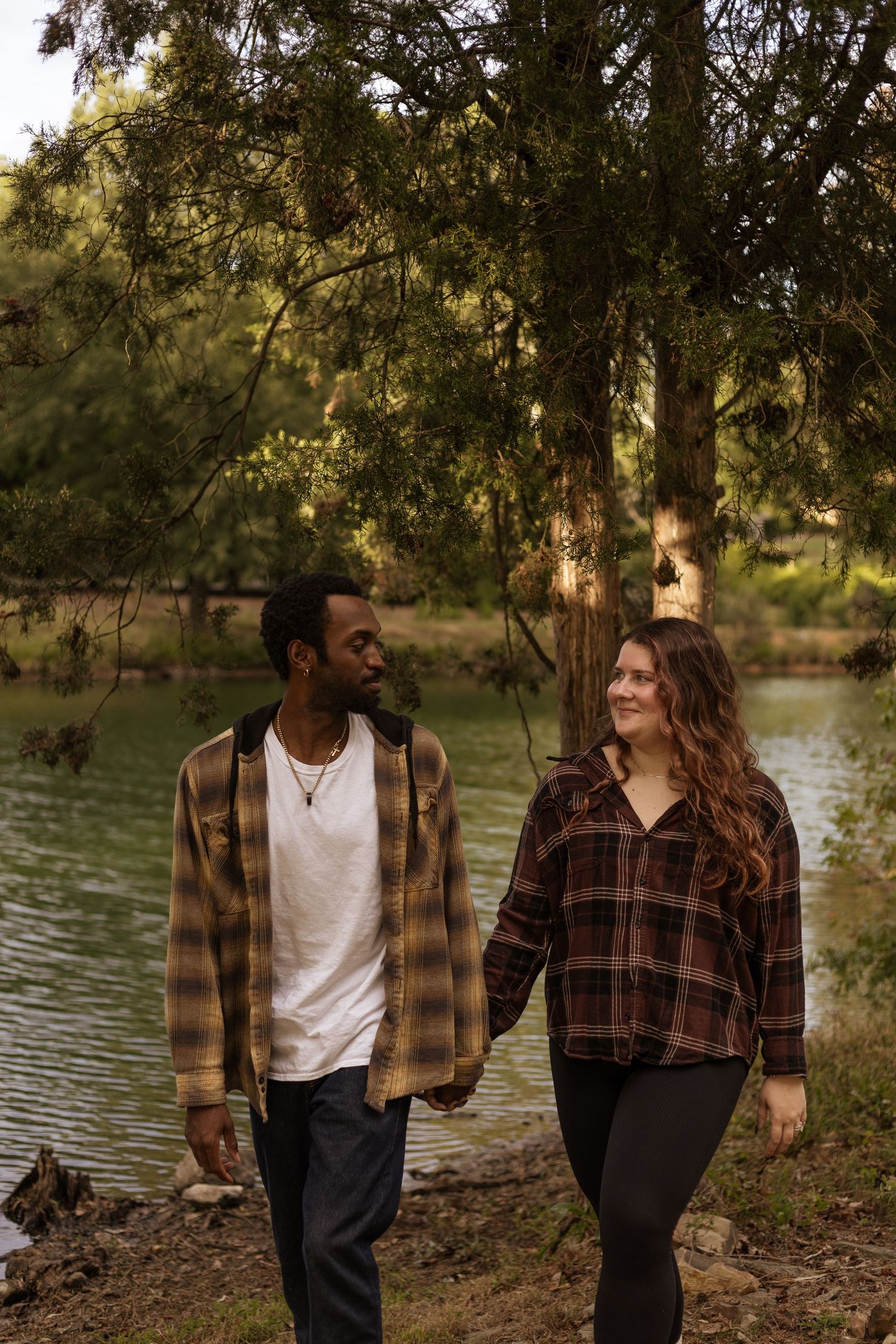 A couple shares a romantic moment by a lake while wearing coordinating brown plaid and white outfits in autumn.