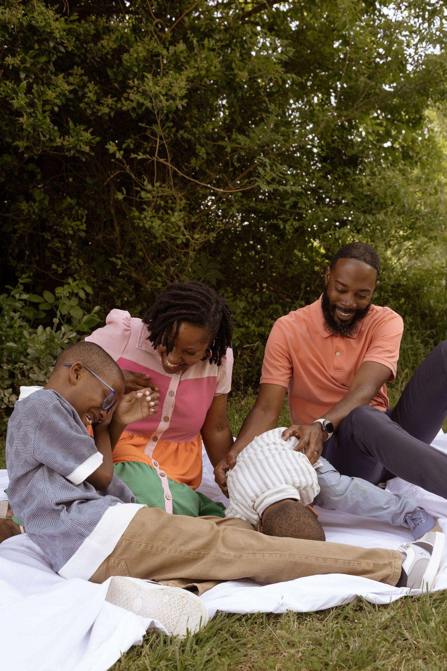 Eight people lie closely together on blankets outdoors while reading books in a garden setting.