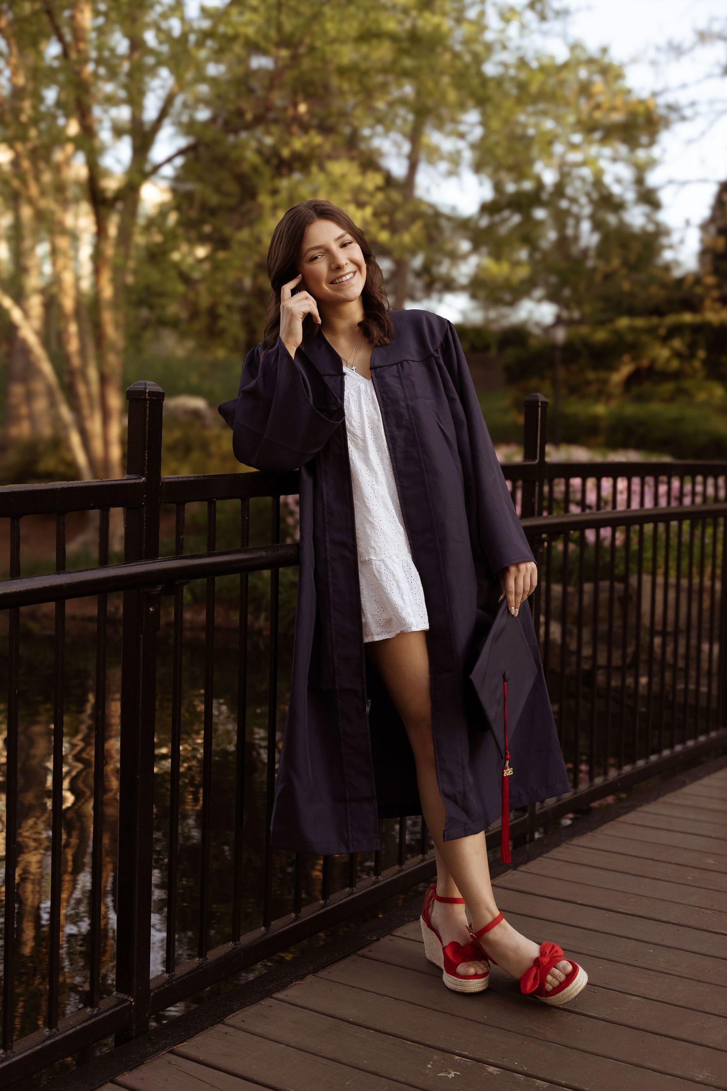 Person wearing a navy coat and bright red shoes poses on a wooden deck during golden hour.