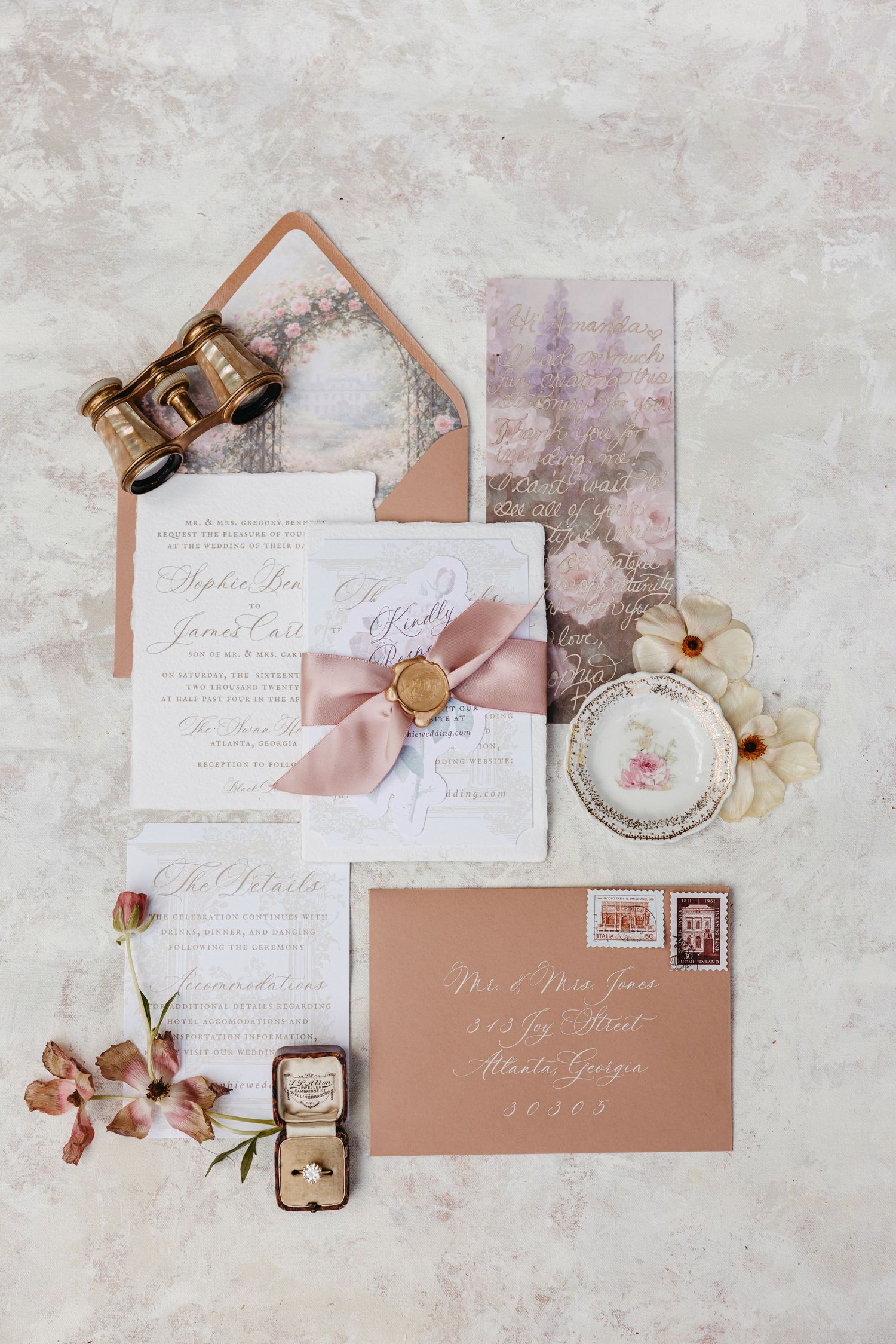Elegant wedding invitation suite with dusty rose ribbon, wax seal, floral envelope liner, vintage binoculars, and kraft envelope flatlay.