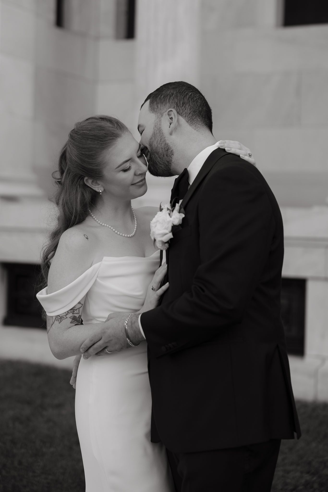 A couple shares a romantic moment in black and white as the bride in an off-shoulder gown embraces her groom.