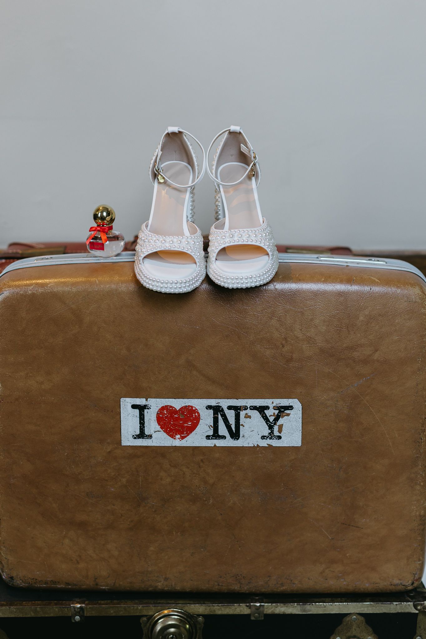 White wedding sandals sit atop a vintage brown suitcase with an I Love NY sticker on the front.