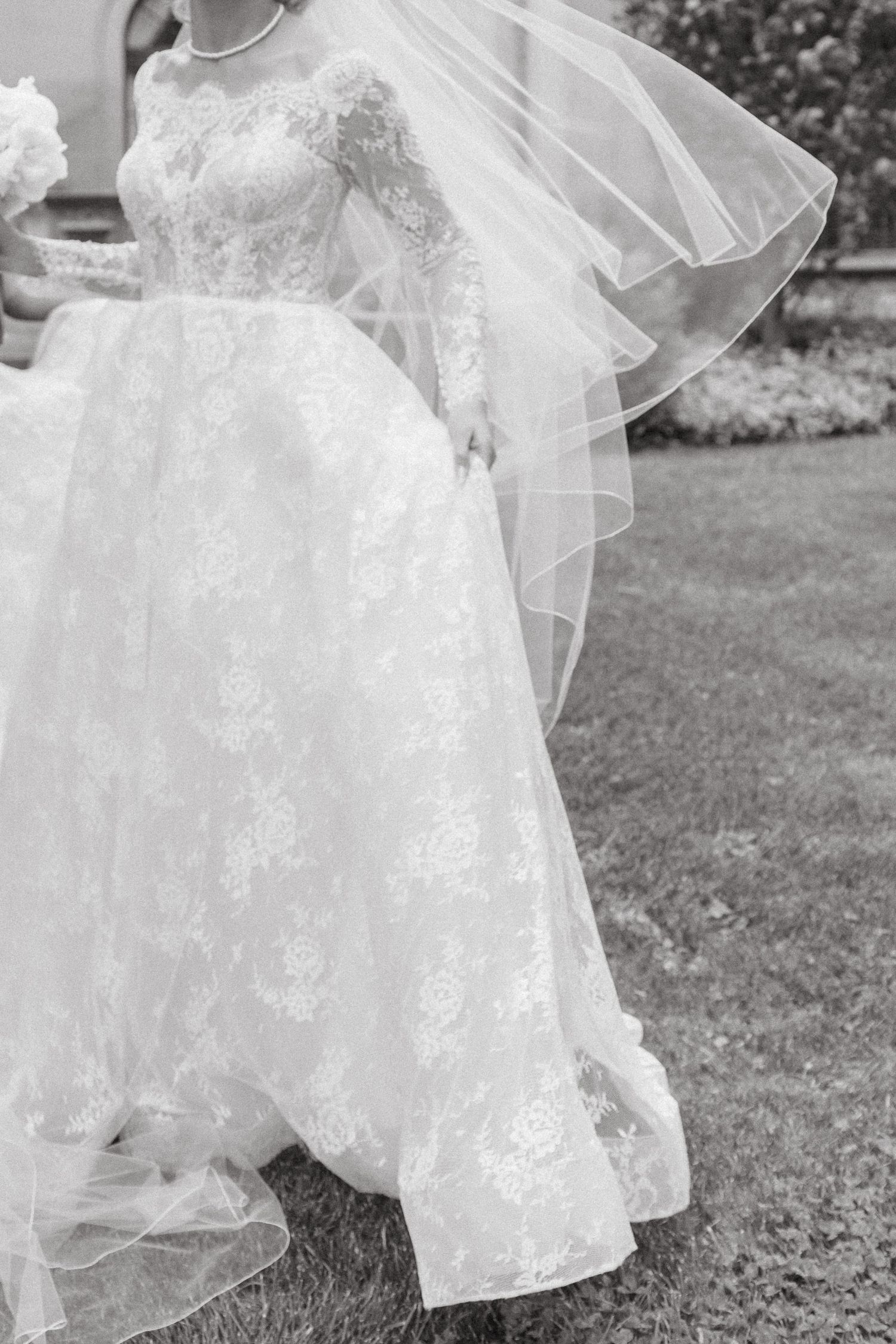 Close-up details of a delicate white lace wedding dress with flowing layers of tulle in an outdoor garden setting.