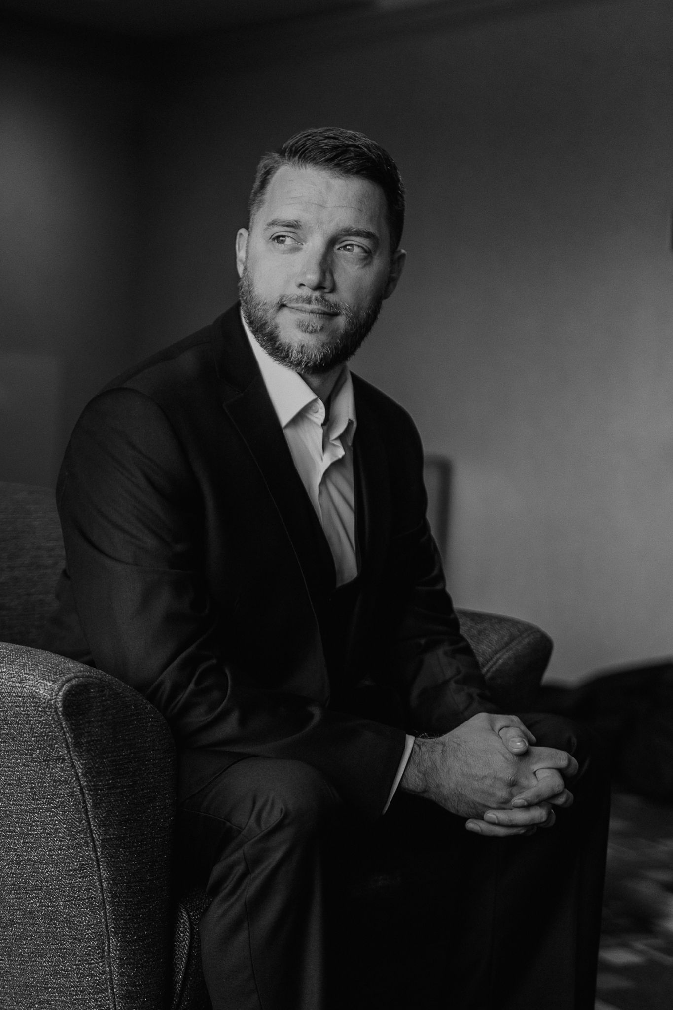 Dramatic black and white portrait series showing a man in a suit posing thoughtfully against dark background.