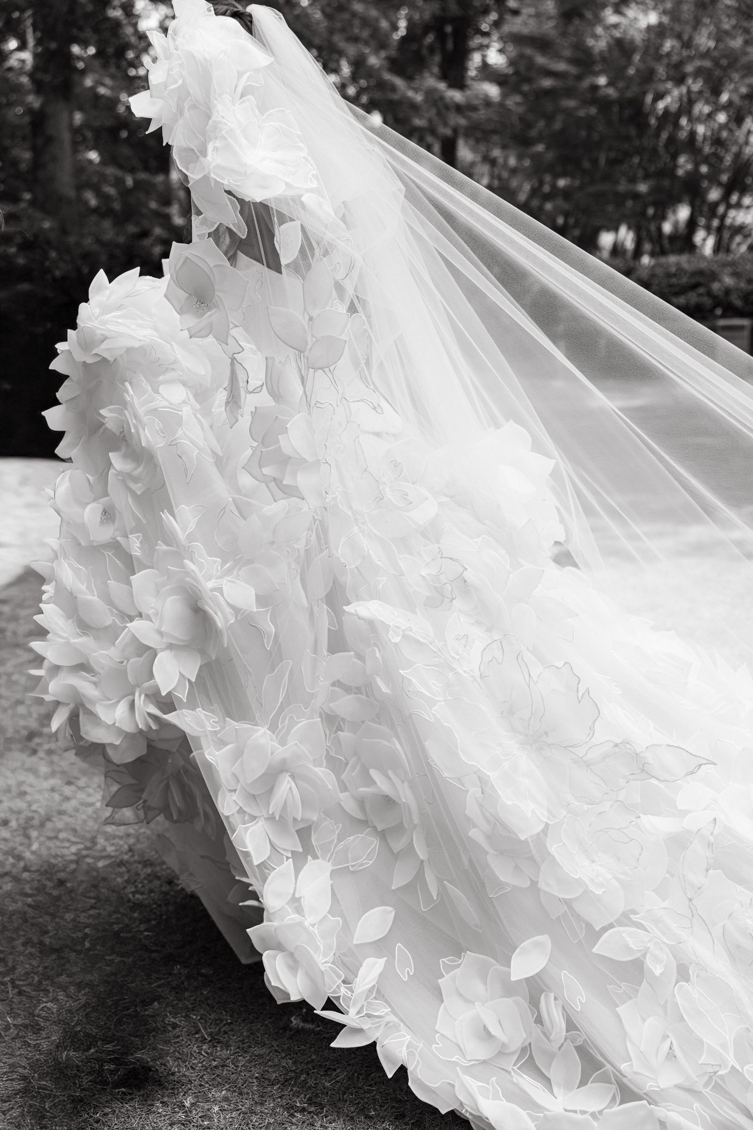 Black and white close-up of a bride's floral appliqué wedding gown and flowing veil with delicate leaf details.