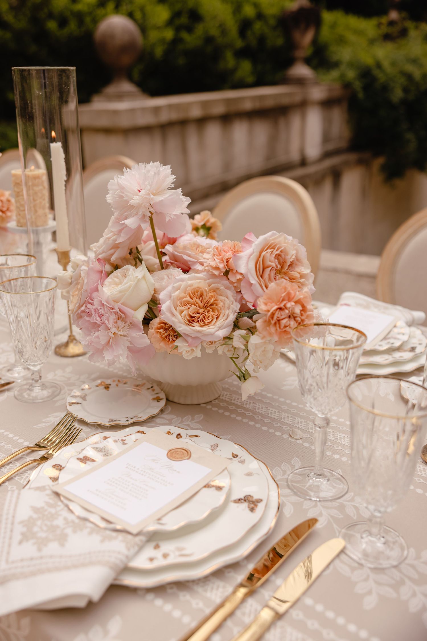 Romantic wedding tablescape featuring blush pink peony centerpiece, gold cutlery, crystal glassware, and ornate white china place settings.