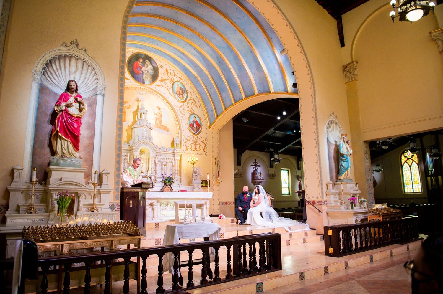Interior panoramic view of a traditional Catholic church sanctuary with ornate altar and arched ceiling decorations.