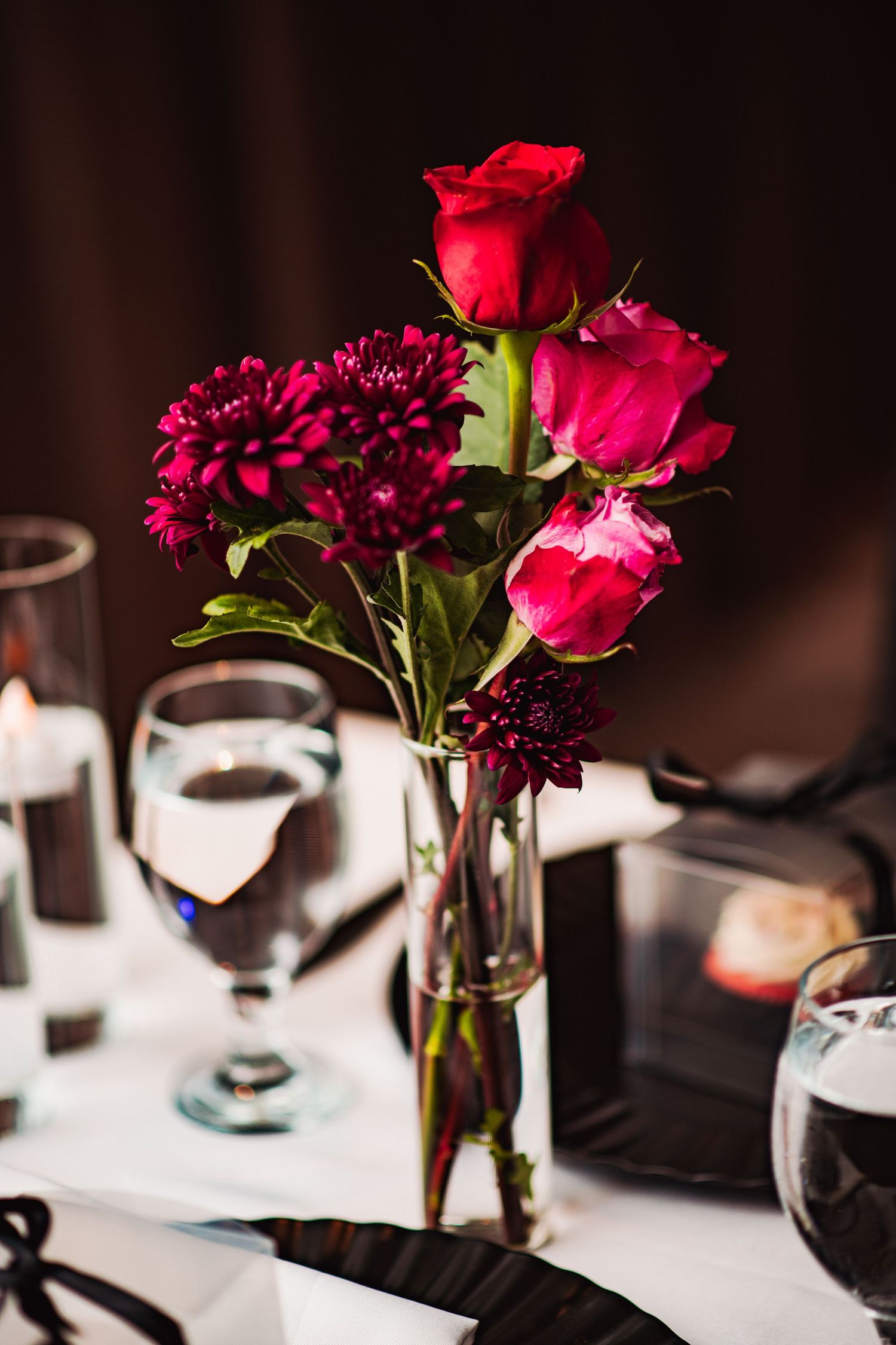 Elegant table settings with deep red roses and burgundy flowers in glass vases at a wedding reception.