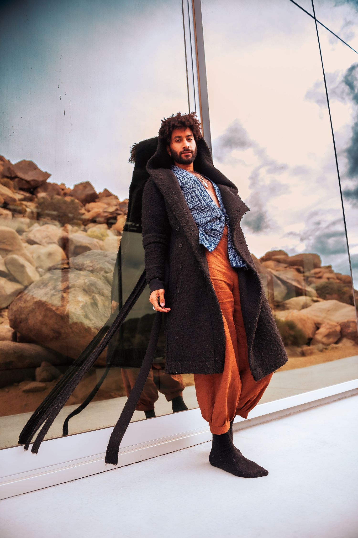 Artistic fashion portrait on white platform against rocky desert landscape backdrop.