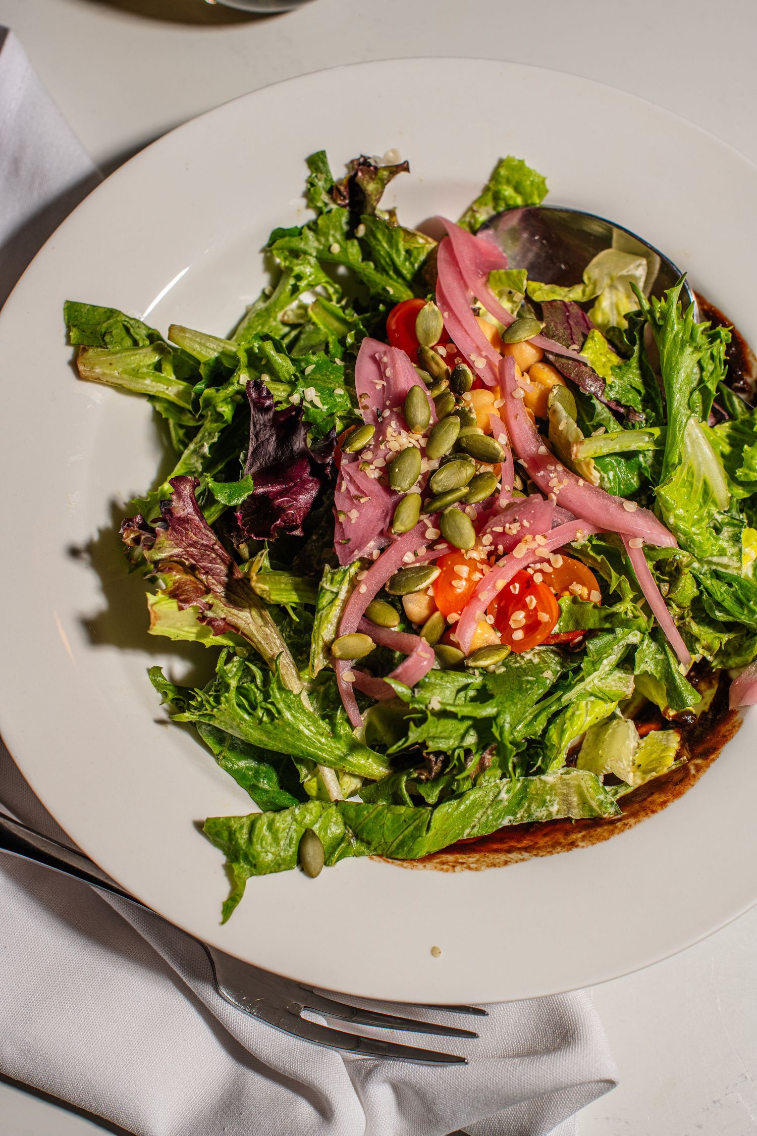 Fresh garden salad with sliced meat and mixed greens served on white plates in a progression of plating steps.
