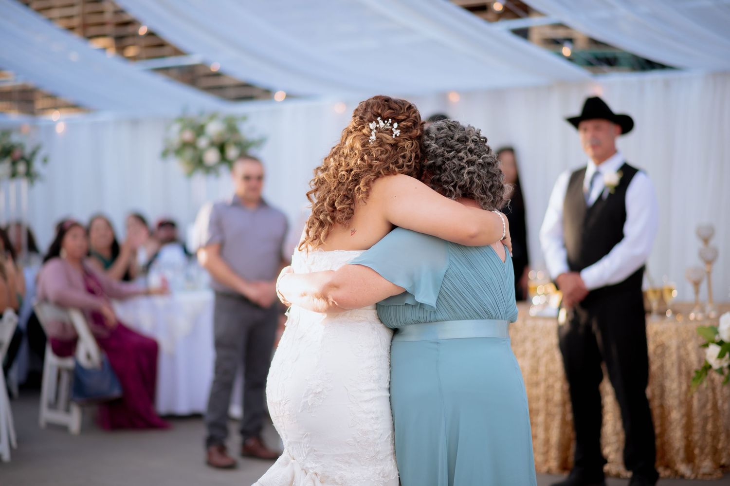 Wedding reception dance with decorative white draping and gold sequin accents in background.