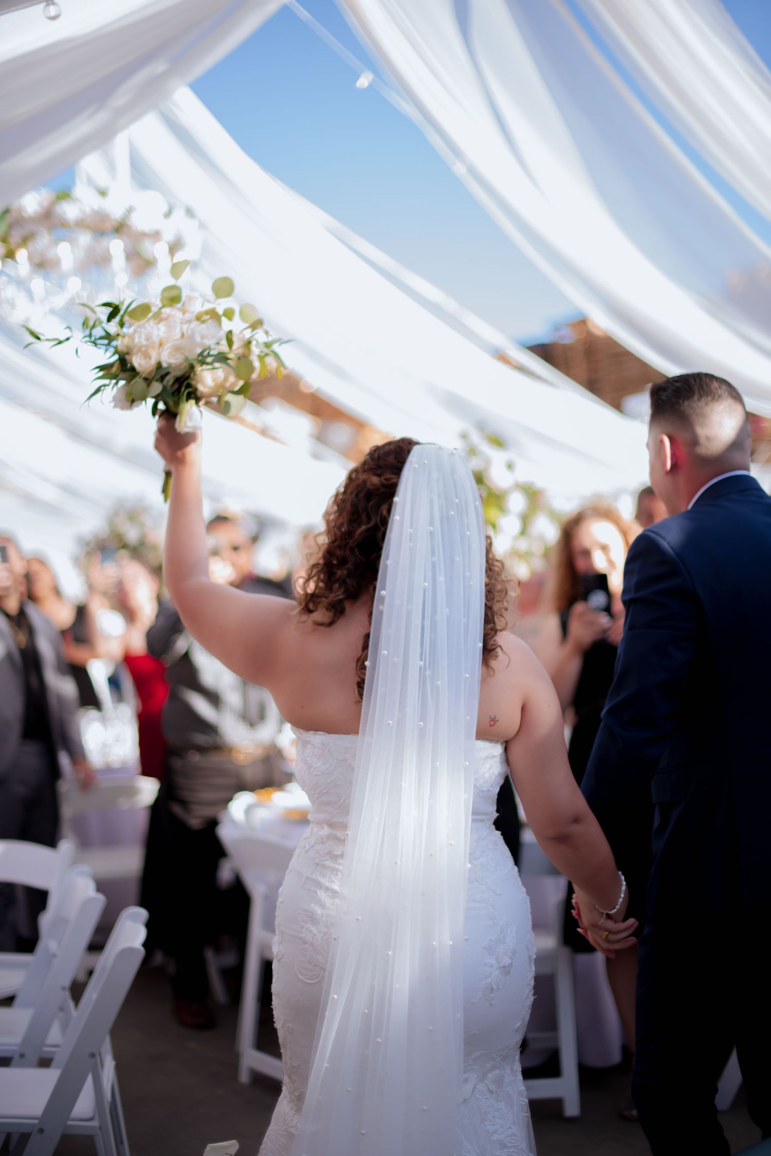 People dancing and celebrating at a wedding reception under white fabric canopy.