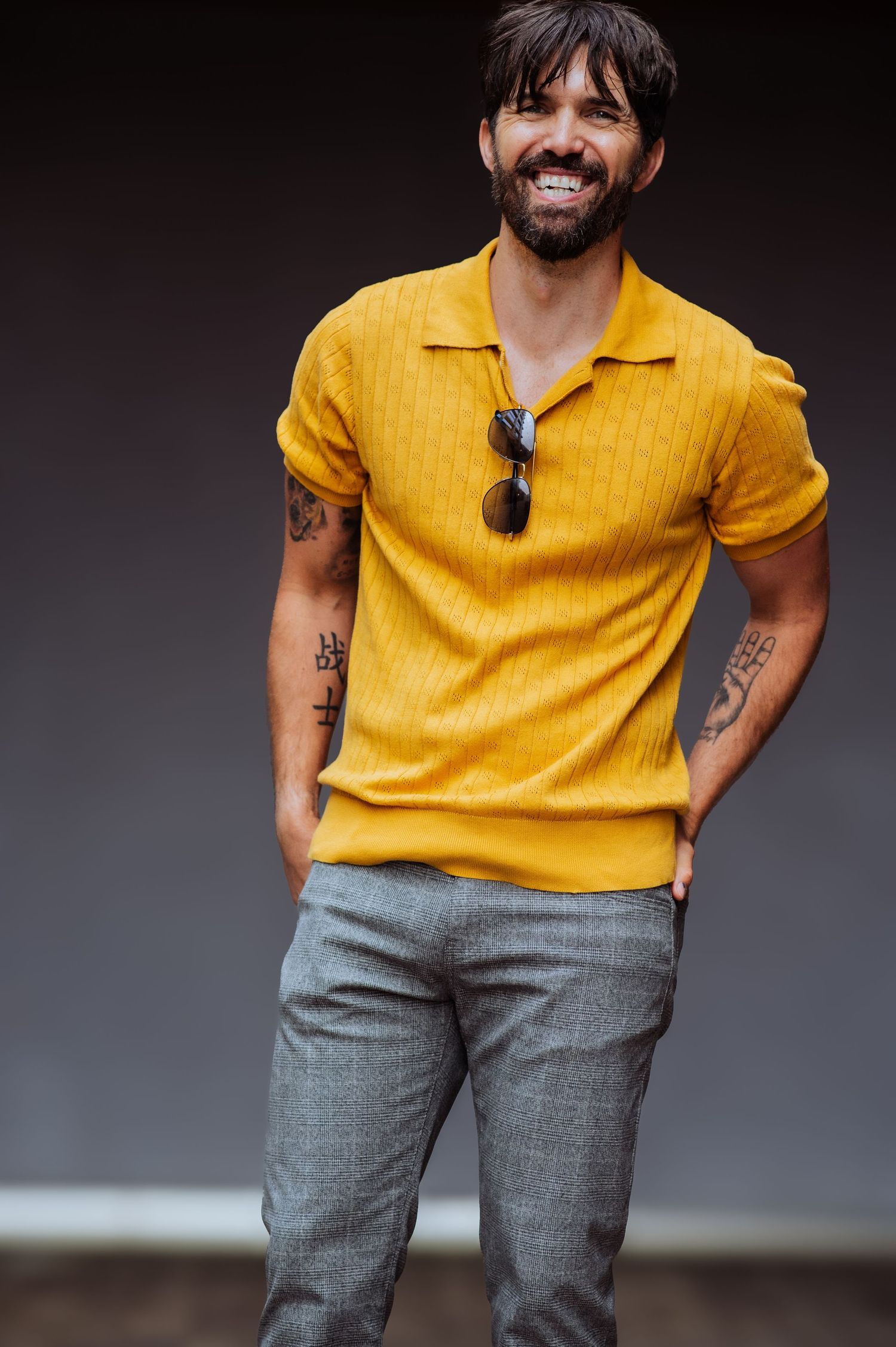 Person in mustard yellow polo and gray pants shows playful attitude in studio setting.