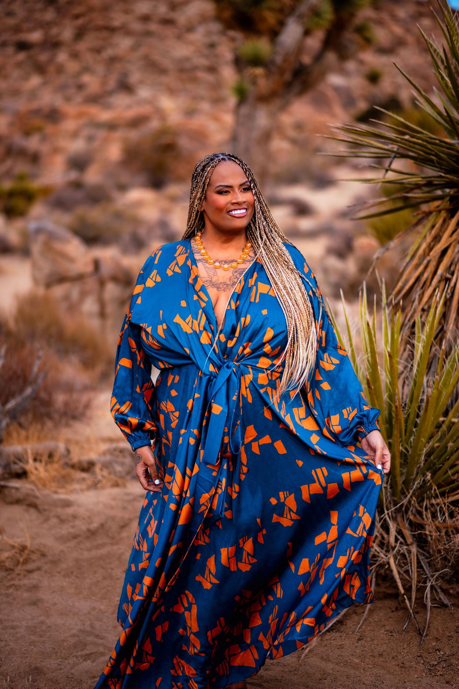 Desert fashion portrait featuring flowing blue and orange patterned dress against mountain landscape.