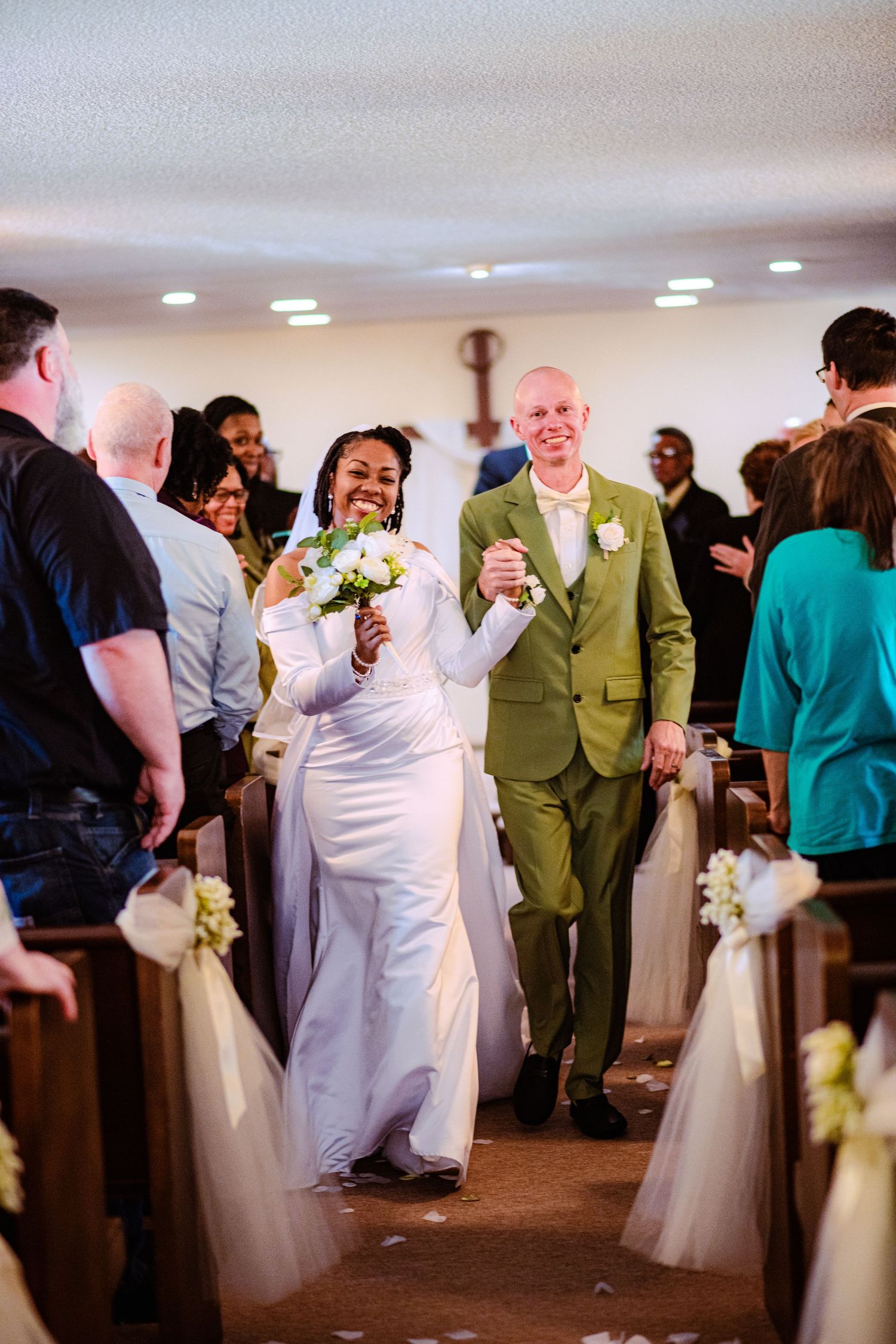 Wedding reception guests mingling and dancing in a bright indoor venue with white and green decor.
