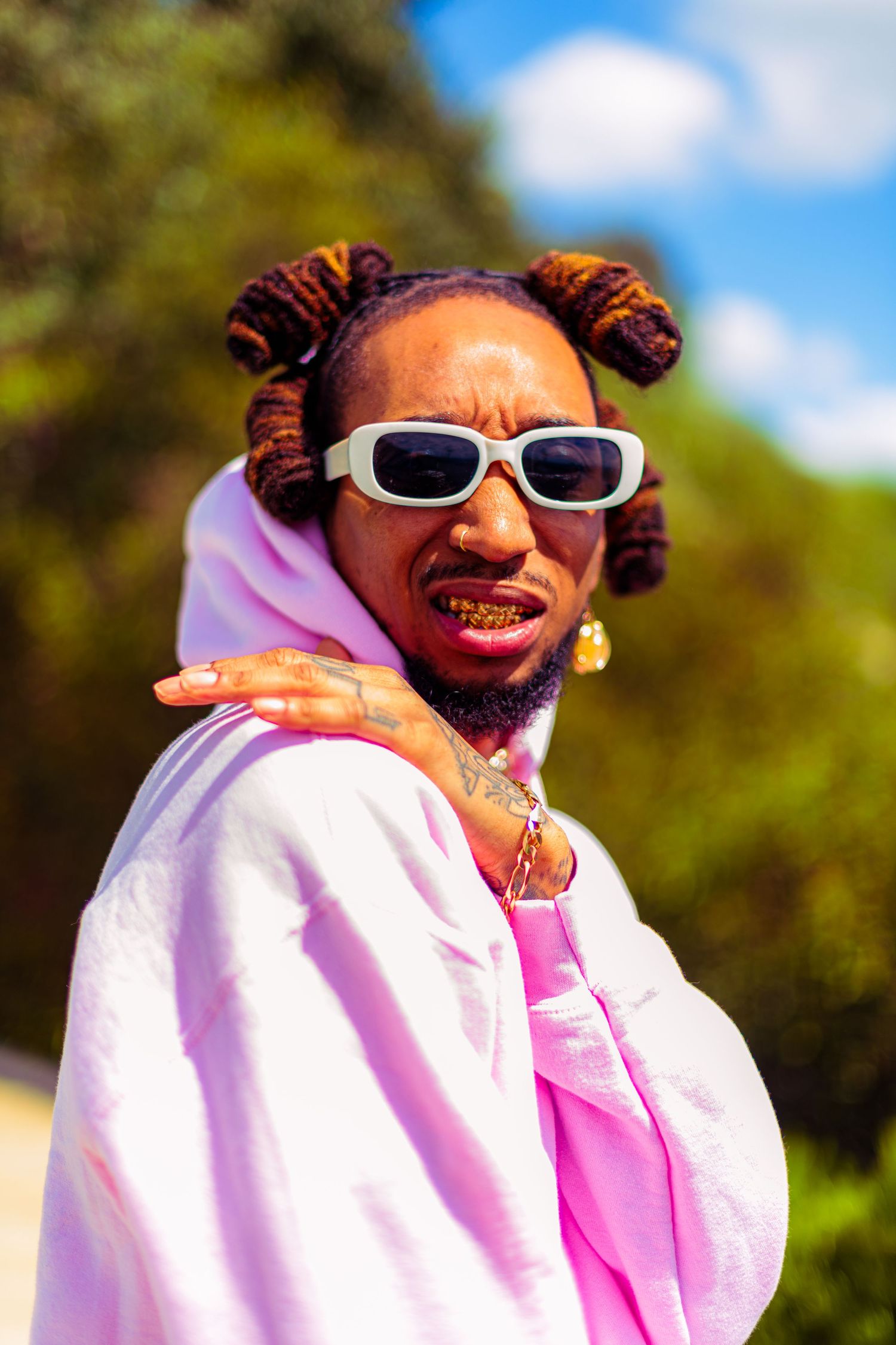 JEFF K%NZ | Recording Artist & Painter Portrait of person in pink hoodie and white sunglasses smiling outdoors on sunny day.