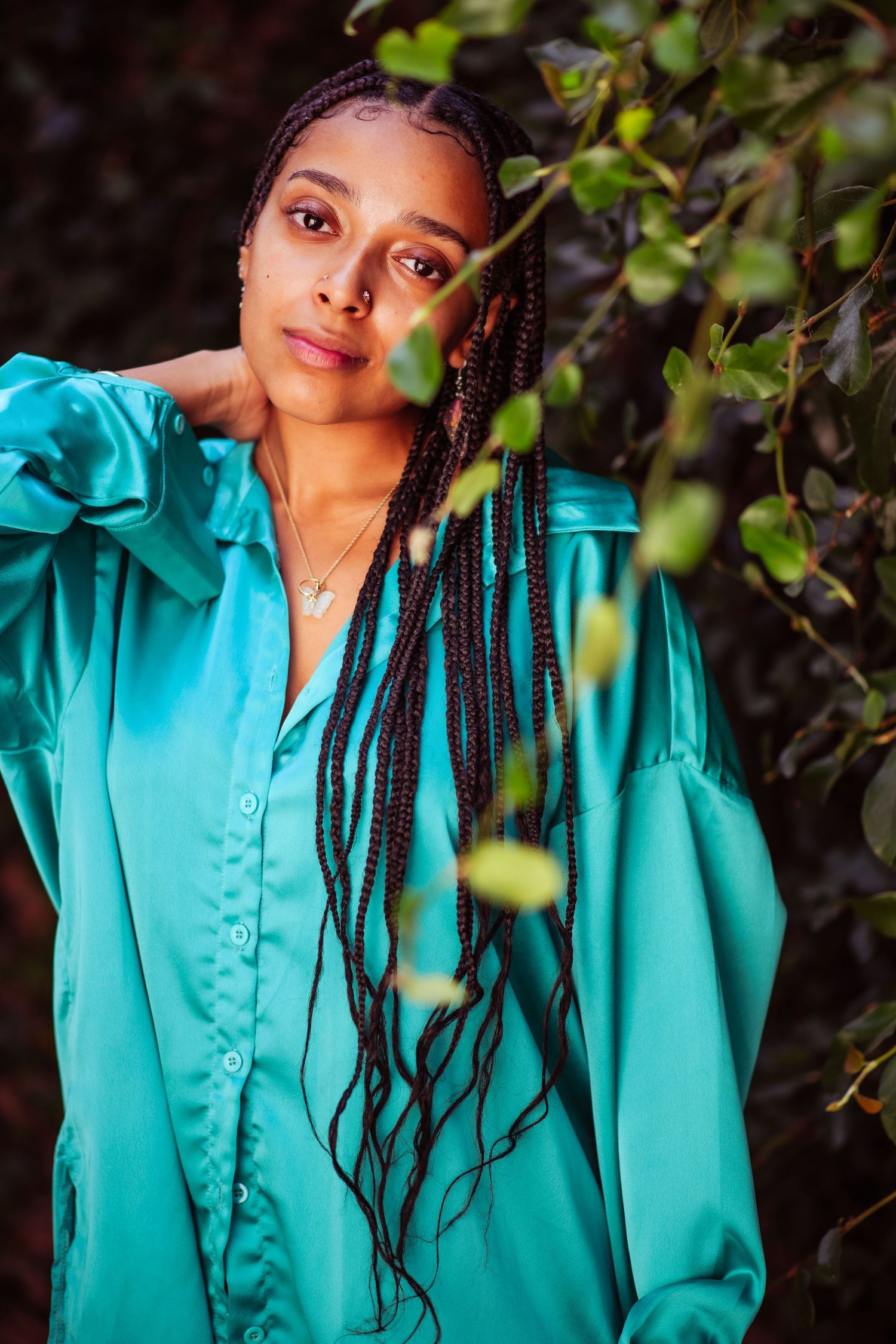 Portrait series showing person in teal button-up shirt posing against green foliage background.