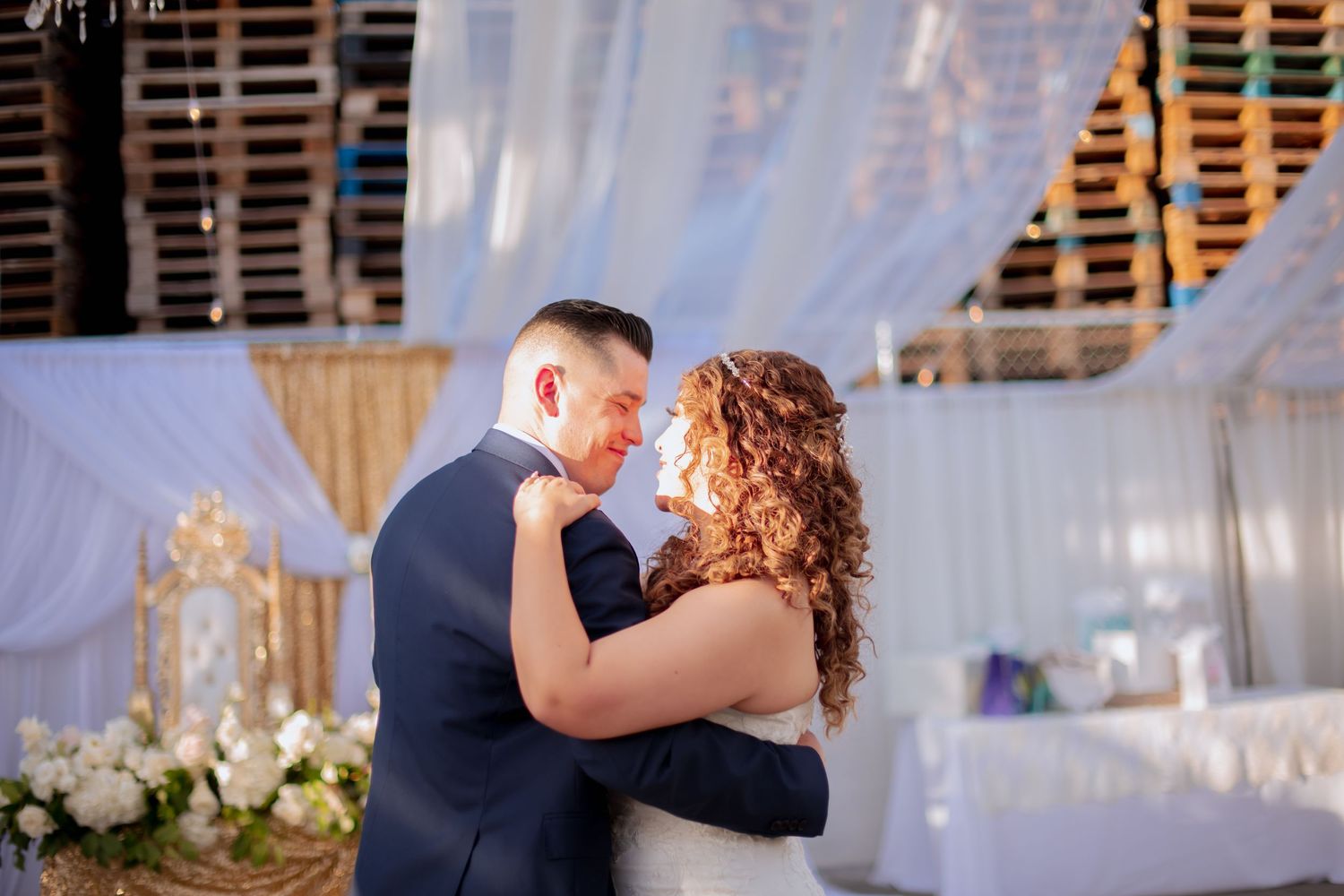Couple dances beneath white fabric draping and decorative lighting at their wedding celebration.