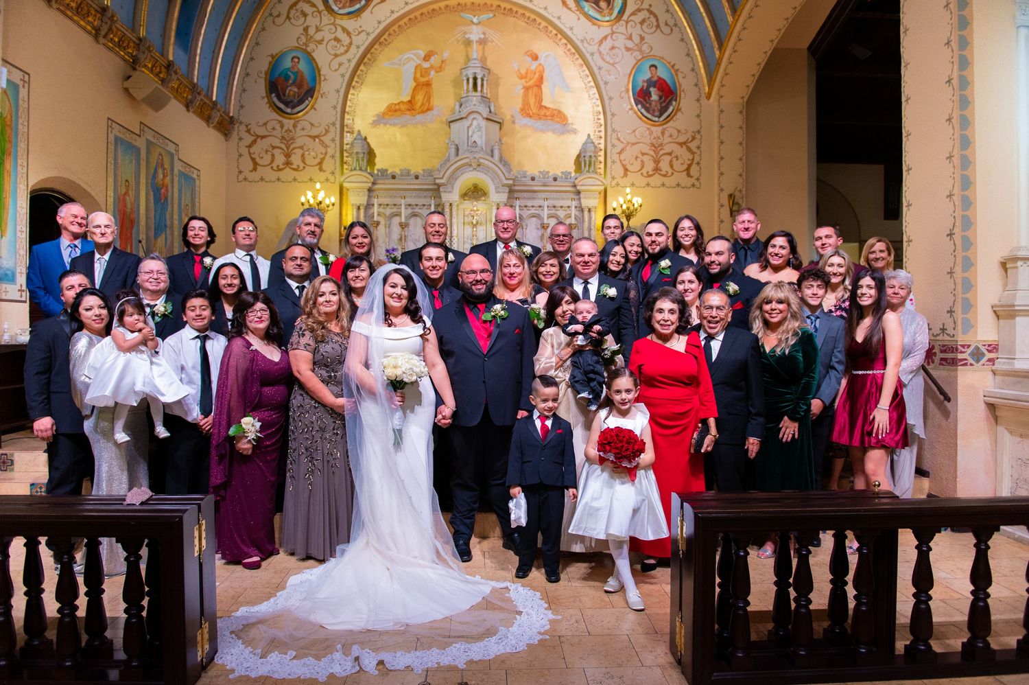 Large wedding party group photo inside ornate church with painted religious murals and arched ceiling.
