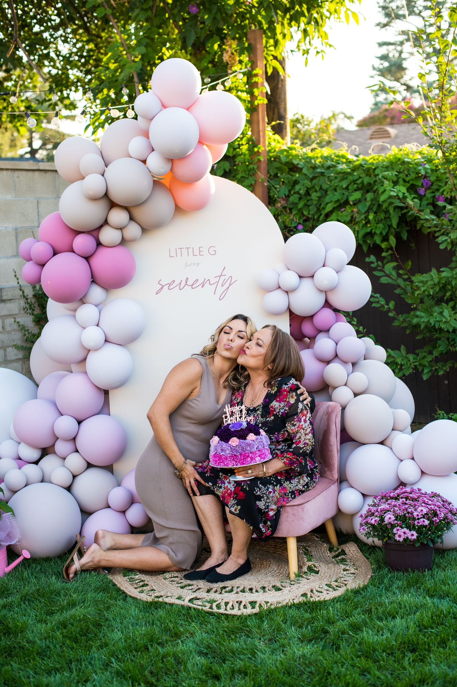 Elegant balloon arch display in pink and white colors set up on grass with decorative boho rug for photo session.