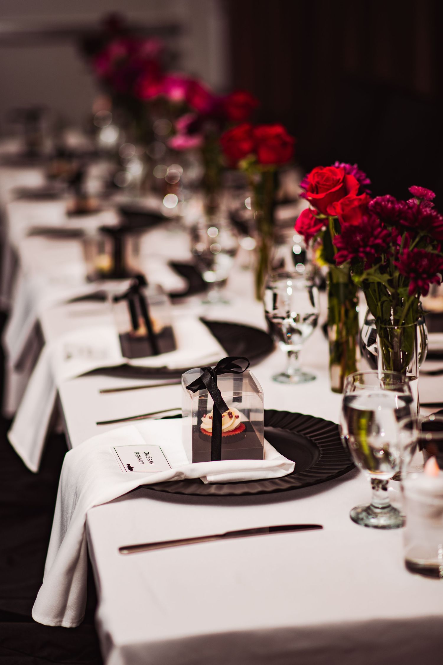 Elegant wedding table settings with red roses and black napkins on white tablecloths.