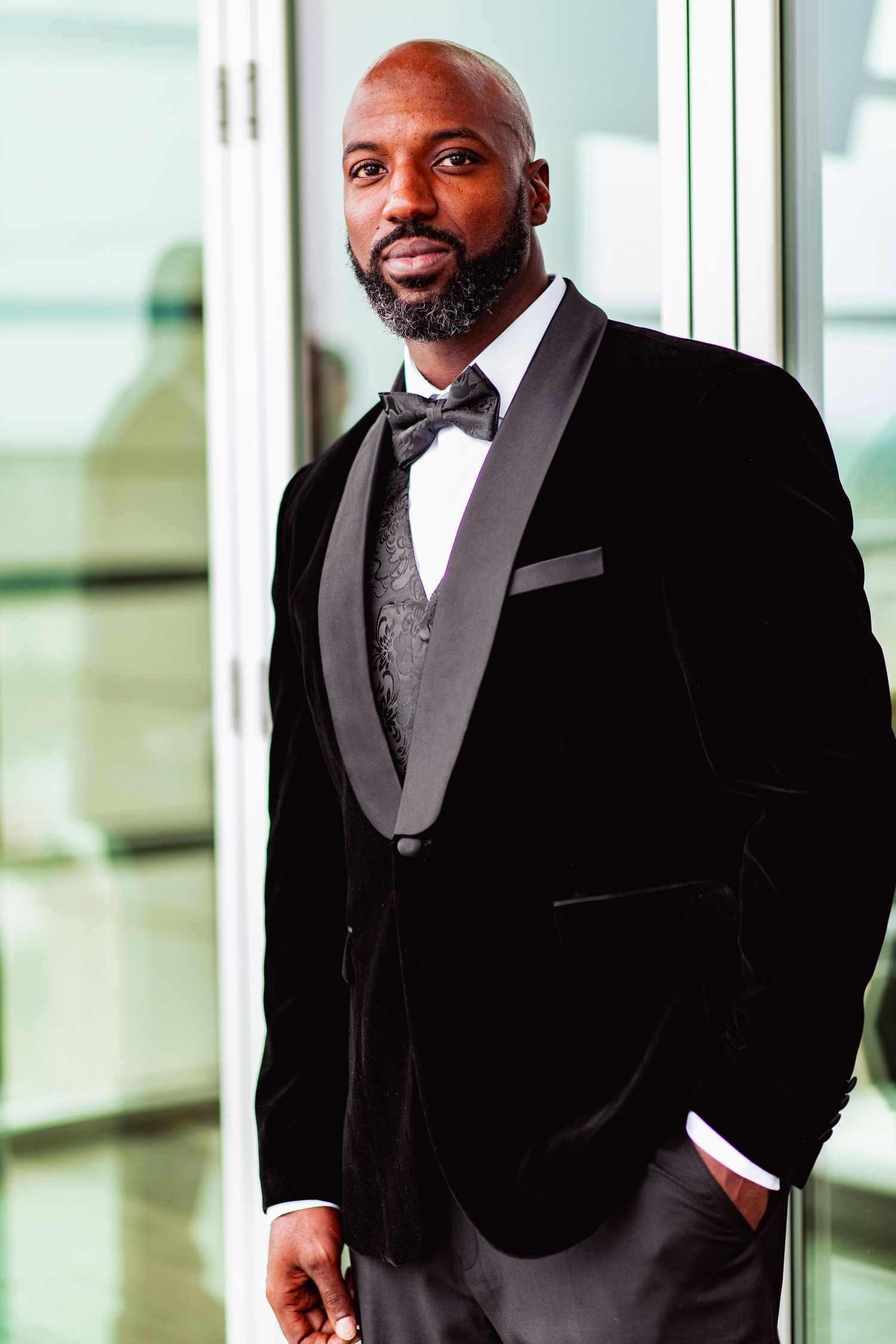 Elegant groomsmen in black tuxedos and bowties pose near bright windows in a modern venue.