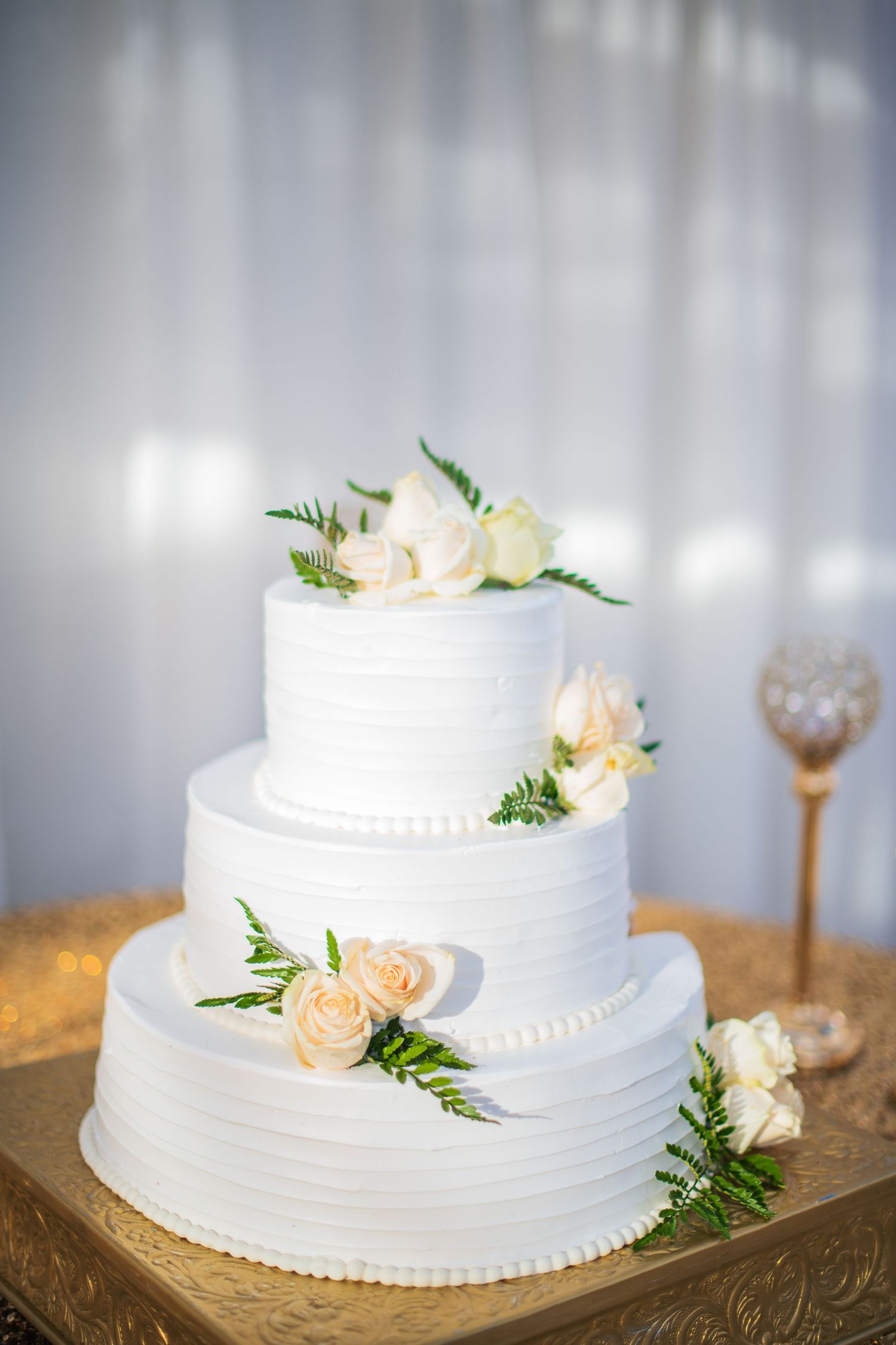 Simple tiered white wedding cake adorned with fresh roses and greenery on a decorative gold platter.