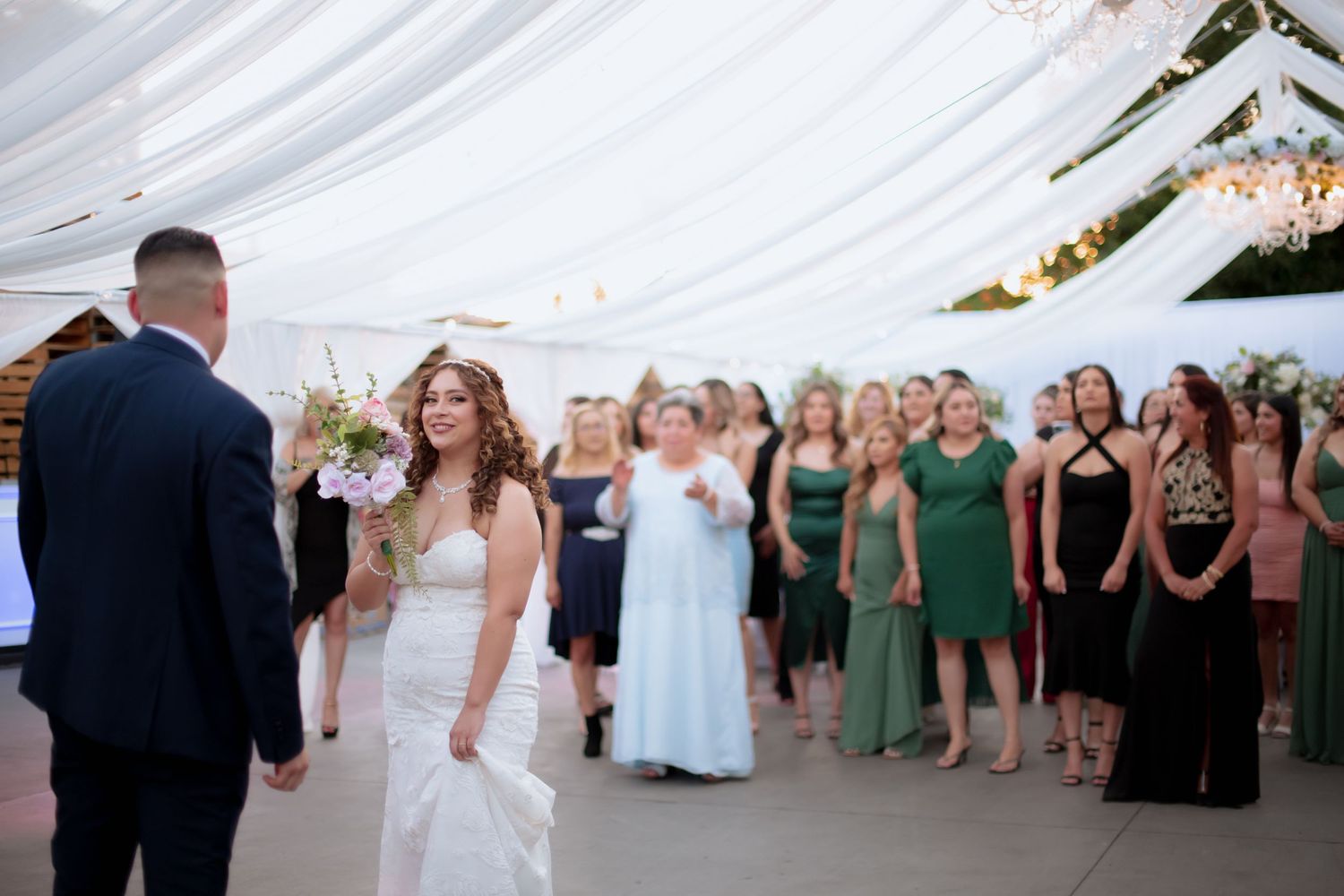 Wedding reception crowd gathered on dance floor beneath elegant white tent decorations.