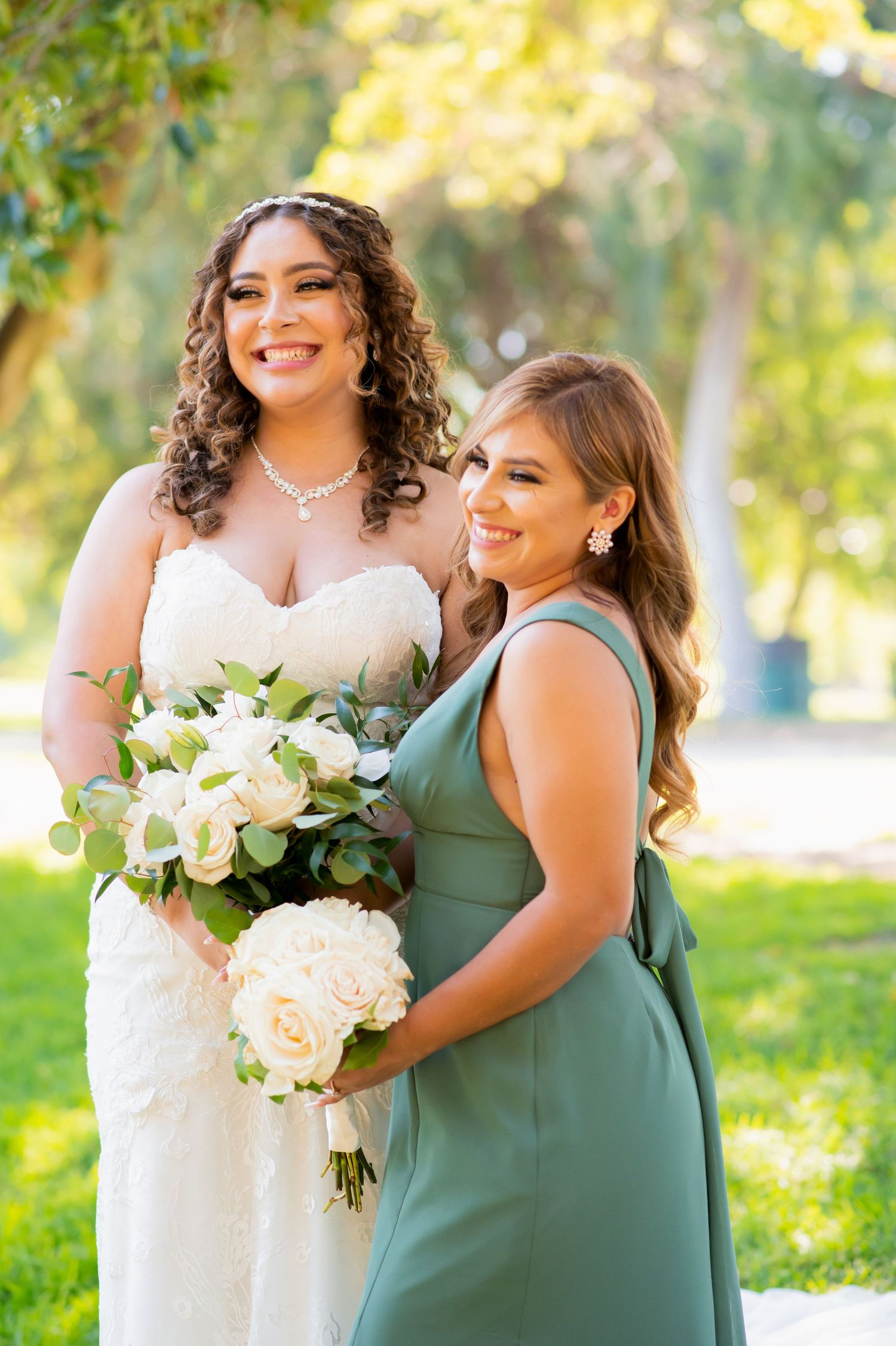 Two members of bridal party share joyful moment while holding white rose bouquets.