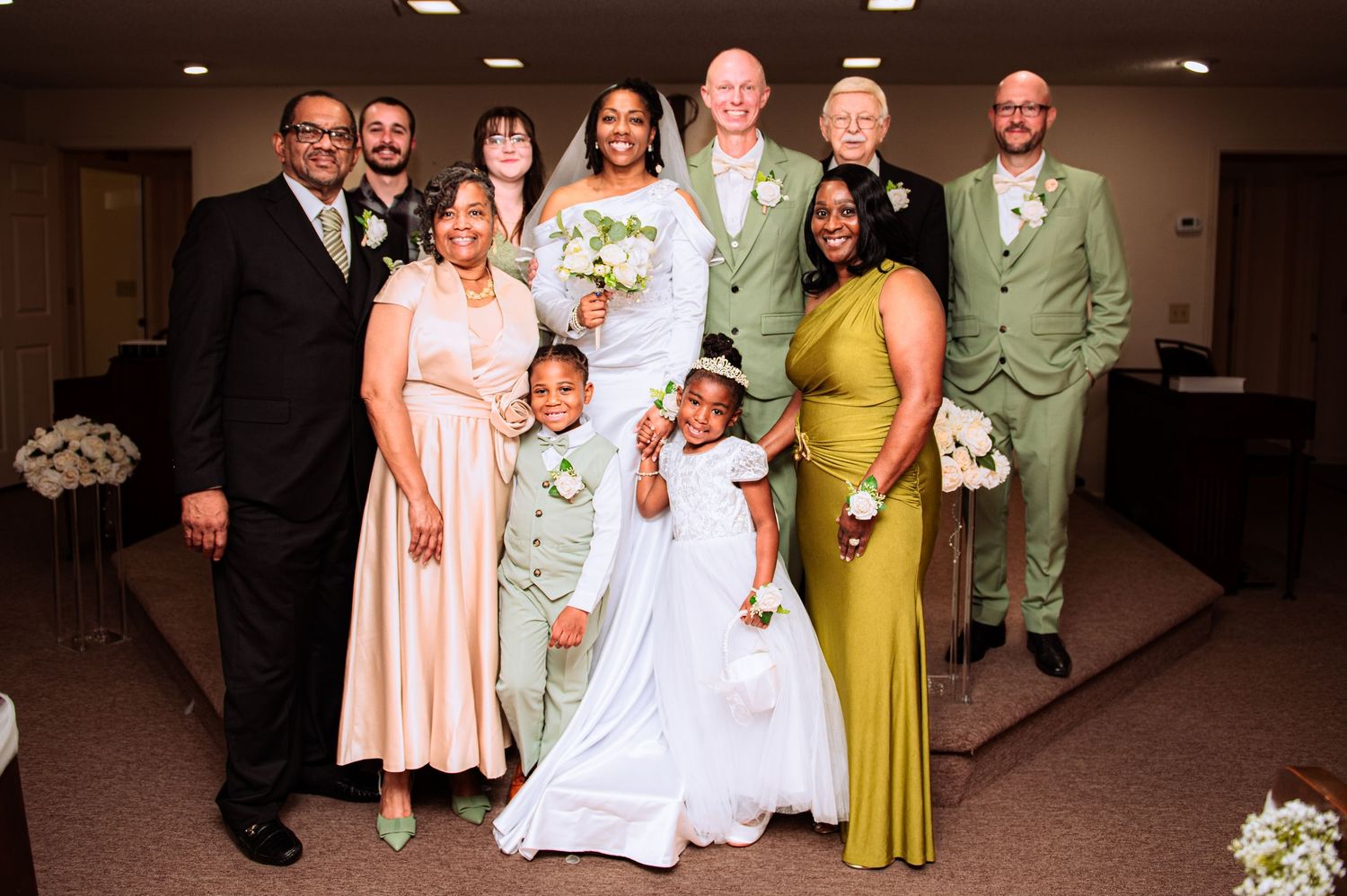 Wedding party poses together in formal attire with the wedding couple in white and green at the center.