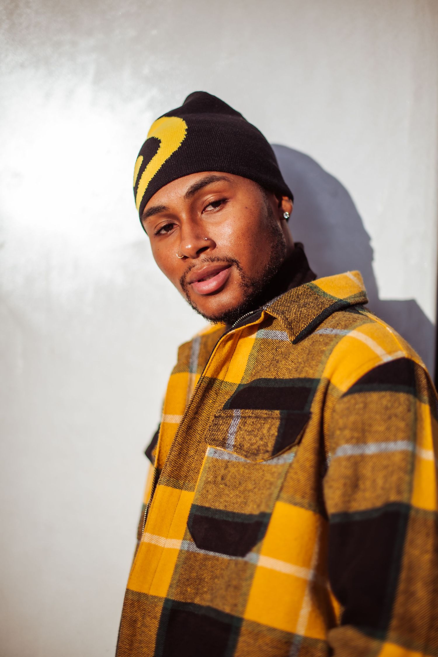 Person in winter attire featuring a yellow buffalo plaid jacket and black beanie smiles at the camera.