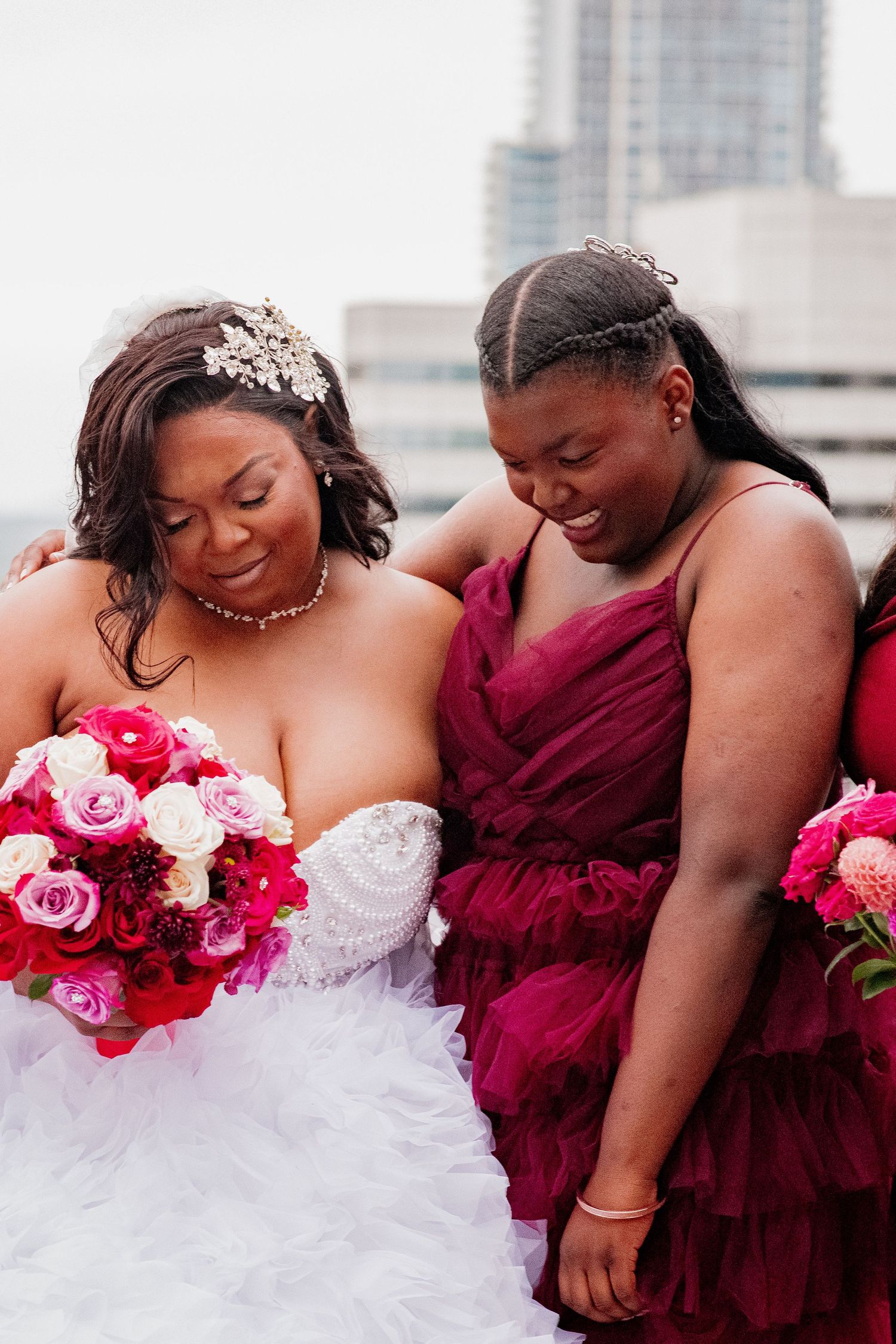 A wedding party in burgundy dresses and white gown pose together while laughing and sharing a joyful moment.