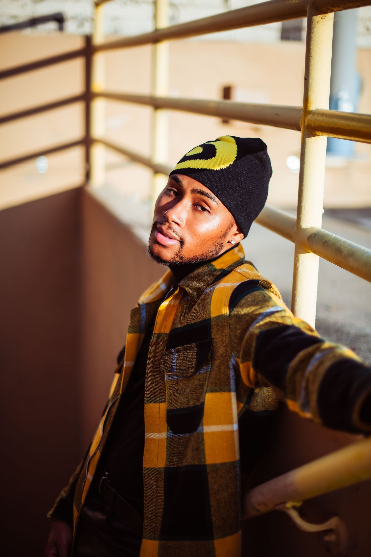 Person wearing a yellow beanie and plaid flannel jacket looks to the side in dramatic lighting.
