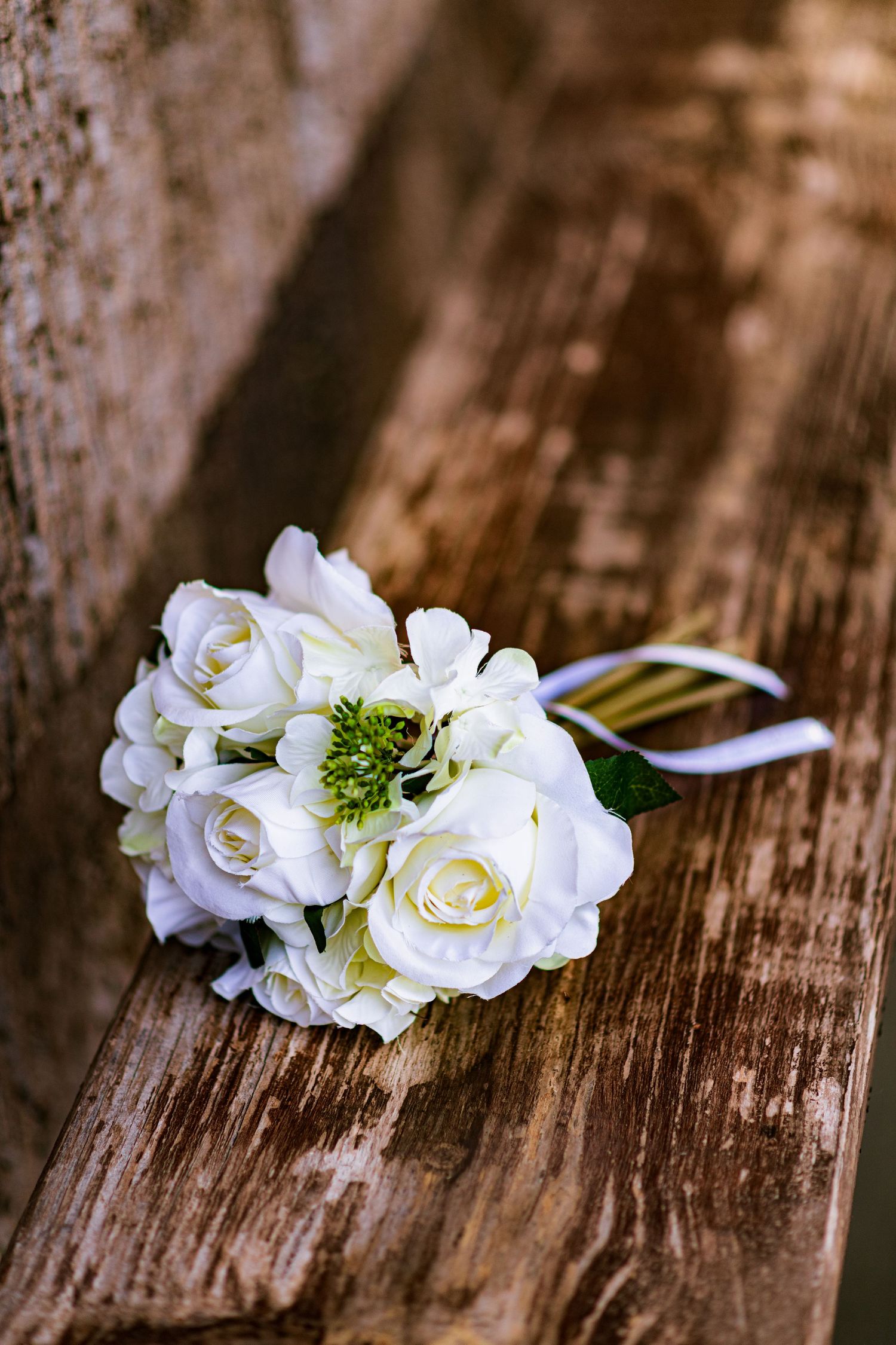 Delicate white roses and greenery arranged on rustic wooden surface.