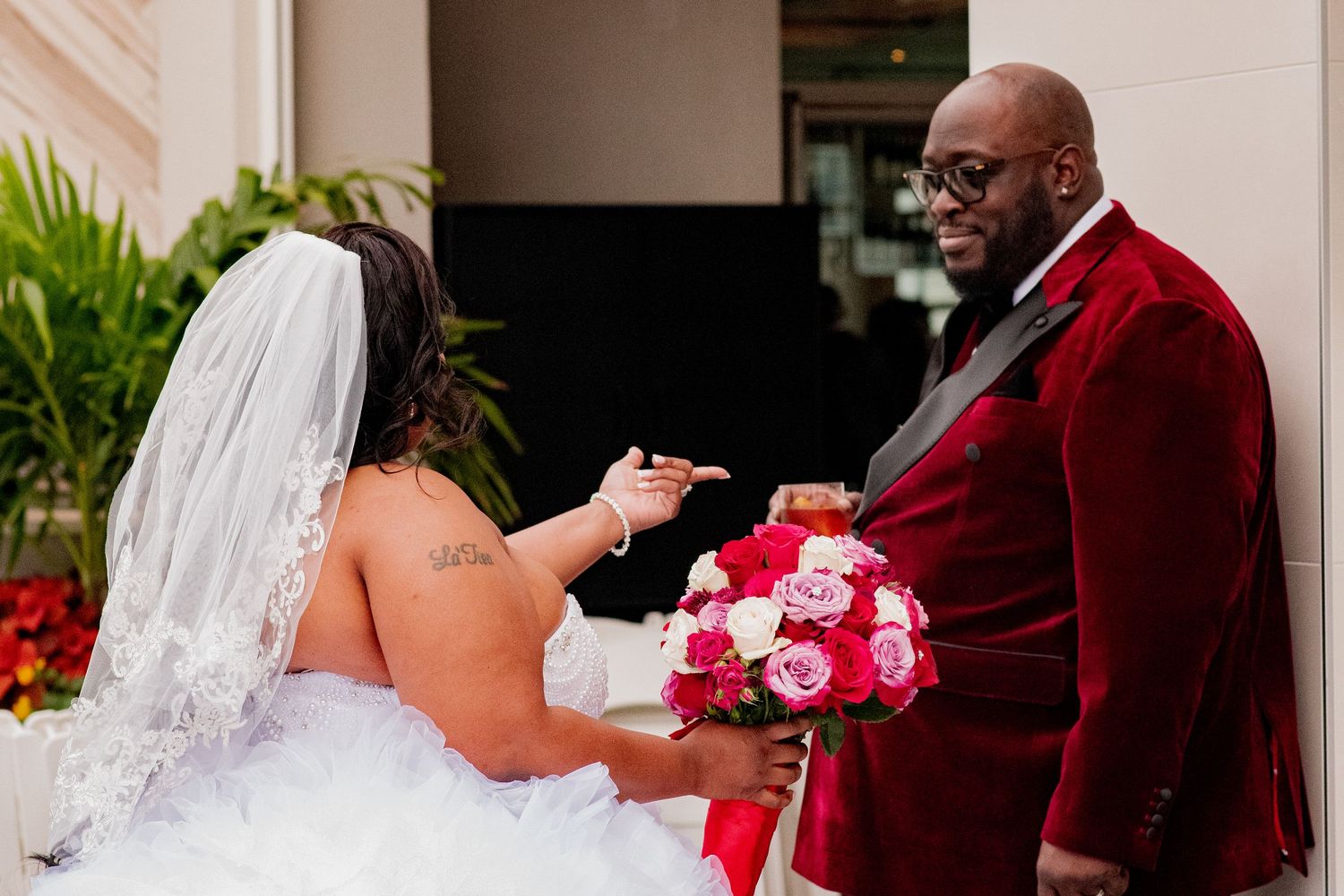 A bride in a white gown exchanges rings with someone wearing a red velvet suit during a wedding ceremony.