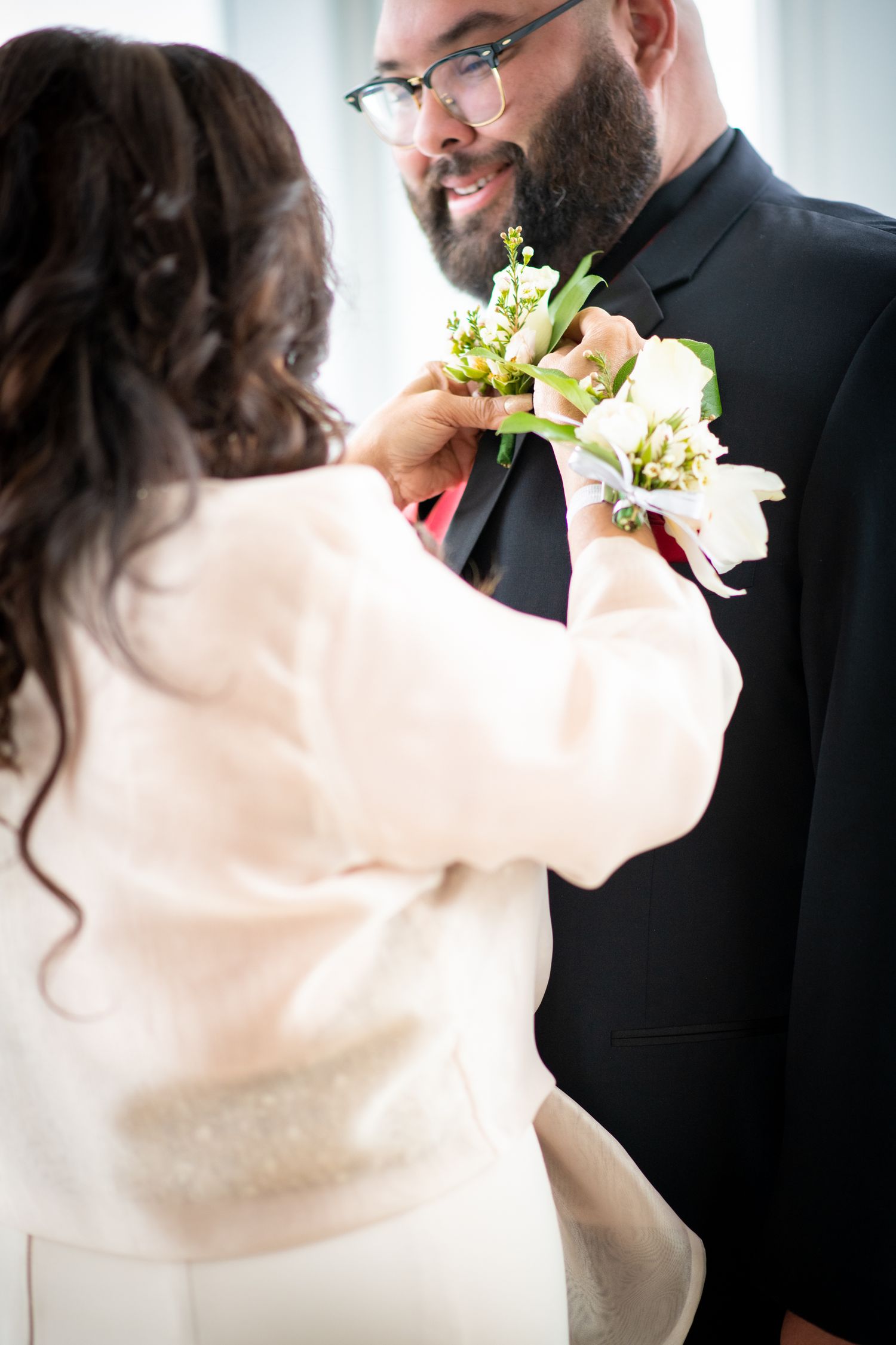 A tender moment as a bride pins a white boutonniere on the groom's lapel during their wedding ceremony.