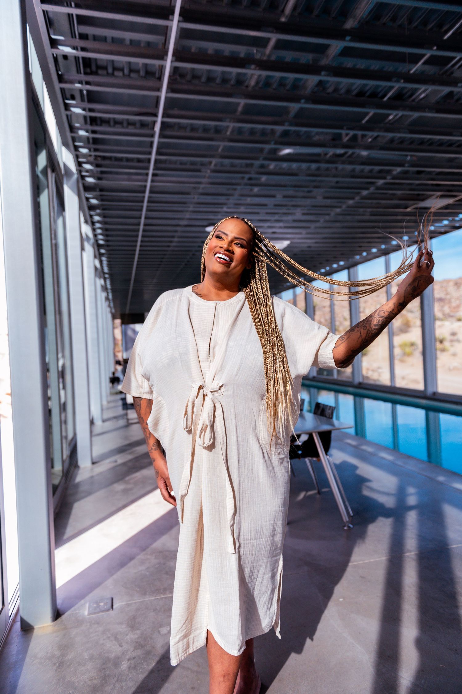 Person in flowing white dress poses joyfully in modern corridor with mountain views.