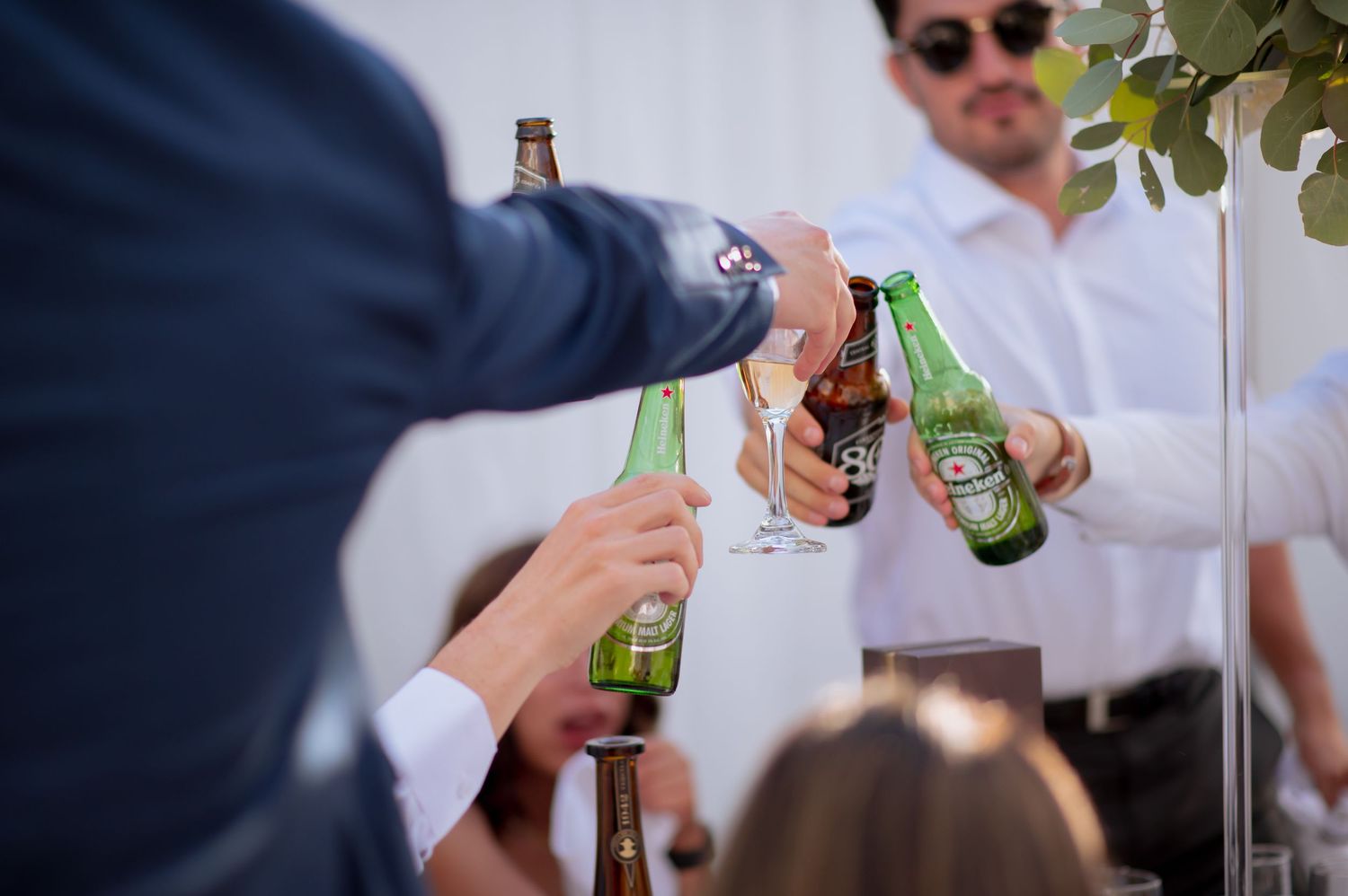 Party guests toasting with beer bottles at an elegant indoor celebration.
