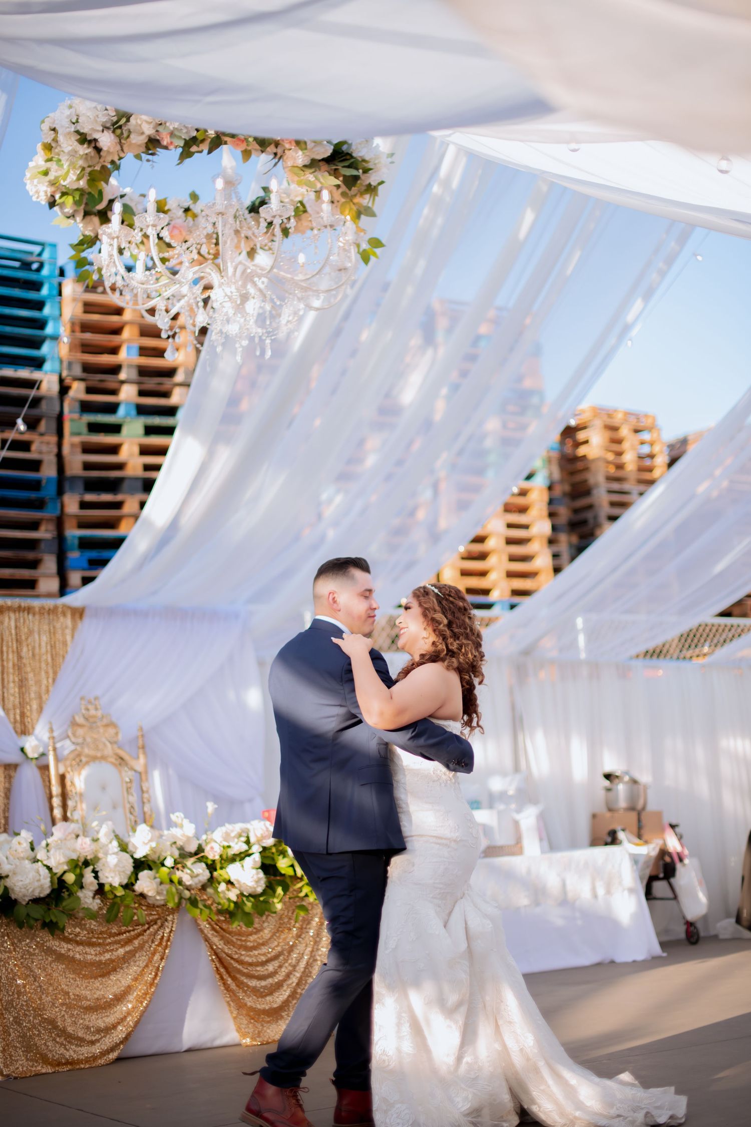 Wedding couple dances together in a venue adorned with flowing white fabric and gold accents.