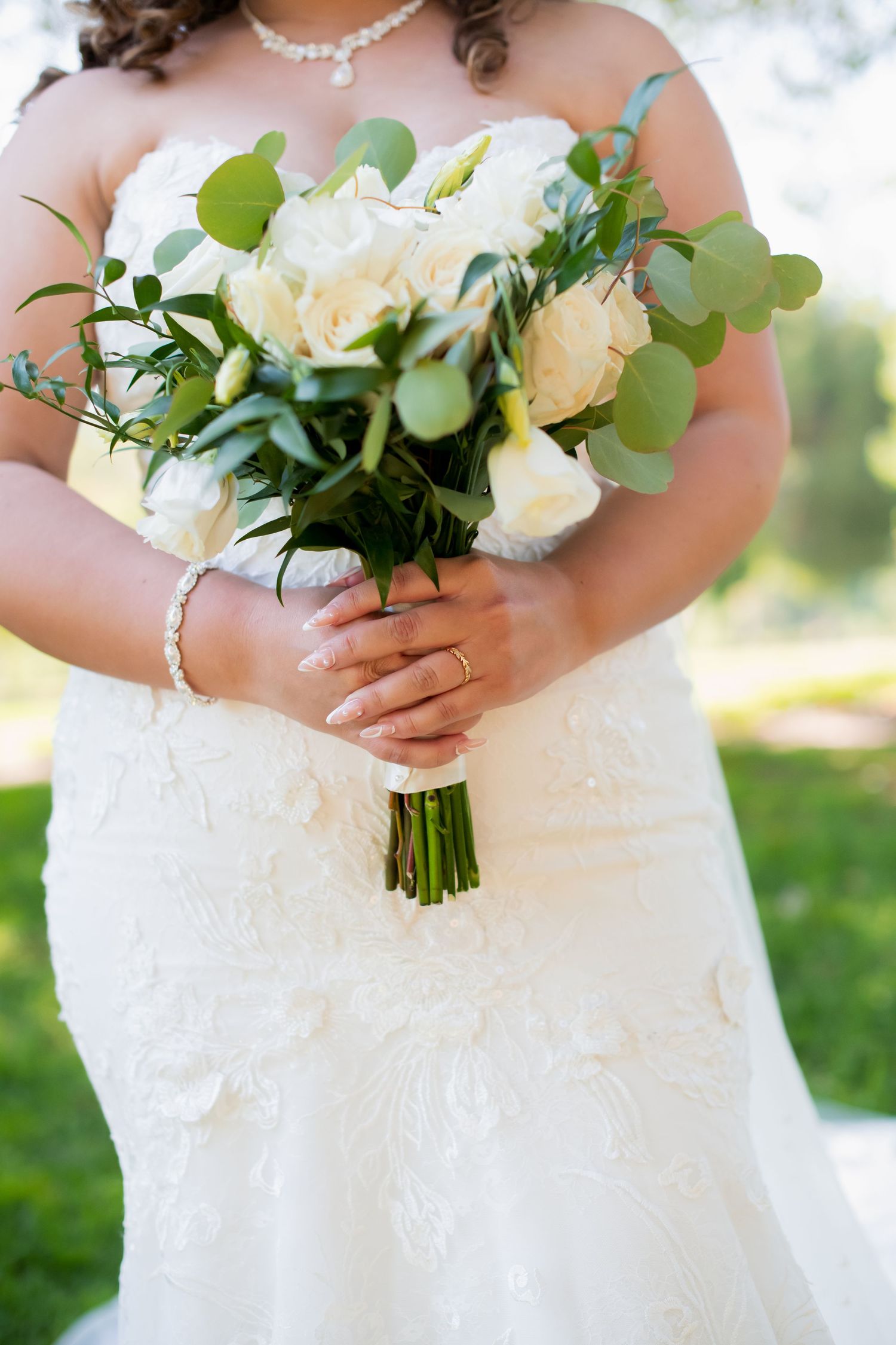 Close-up of white rose and eucalyptus wedding bouquet held by bride in lace dress.