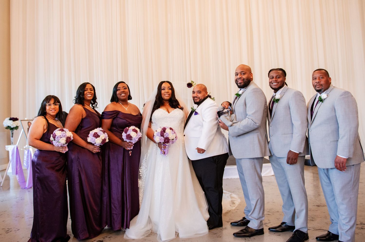 Full wedding party portrait with bridesmaids in purple and groomsmen in gray suits.