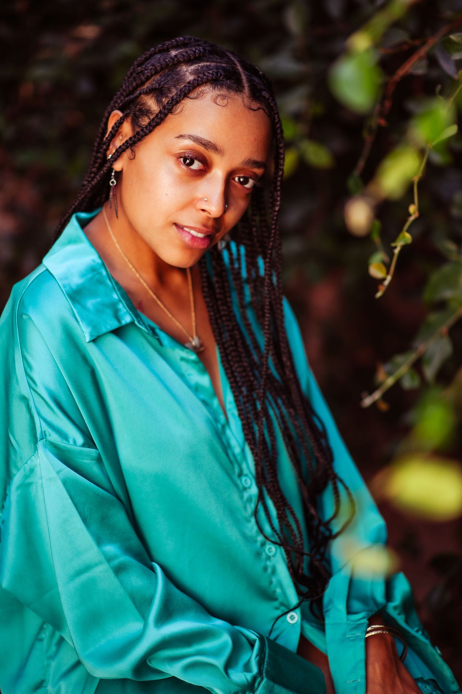 Portrait in turquoise outfit against dark natural background with artistic lighting and bokeh effect.