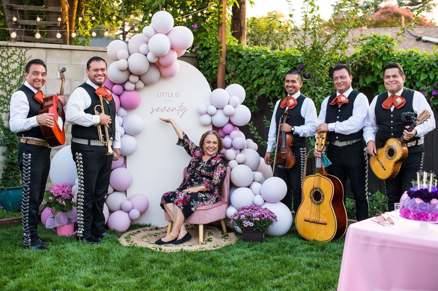 Outdoor celebration with pink and white balloon decorations and musicians playing guitars in a backyard setting.